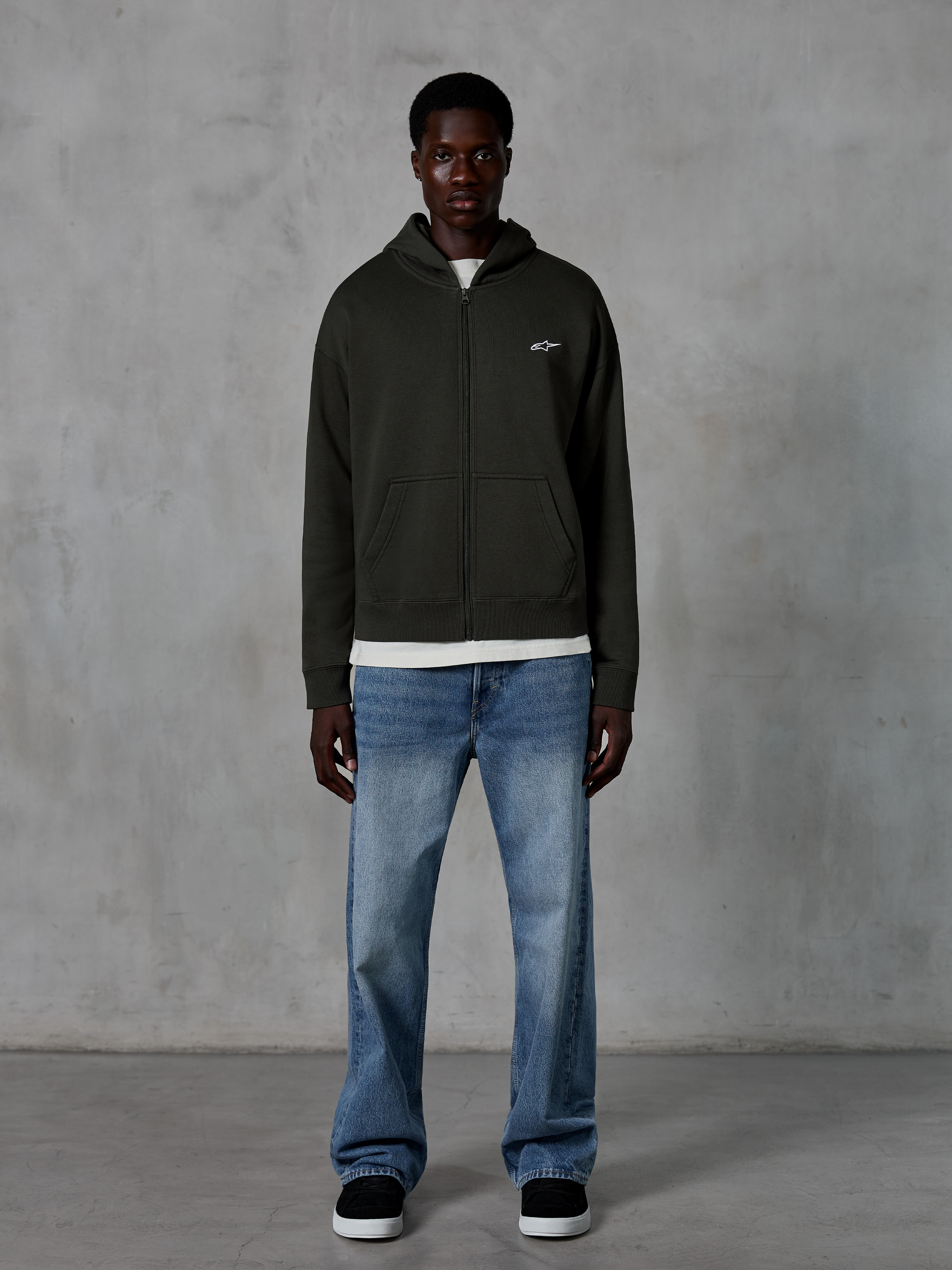 Alpinestars Essentials Ageless Zip Hoodie, hættetrøje med lynlås, Off Black, med et lille hvidt Alpinestars-logo på brystet, båret af en model med hvid t-shirt og blå jeans, afslappet pasform, casual motorsport streetwear