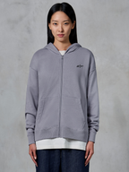 Alpinestars Essentials Ageless Zip Hoodie, Silver, afslappet streetwear, fleece-sweatshirt med gennemgående lynlås, lille sort Alpinestars-logo på brystet, delt kængurulomme, bæres af model over hvid t-shirt og mørke jeans