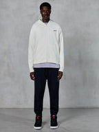Alpinestars Essentials Ageless Zip Hoodie, off-white hættetrøje med gennemgående lynlås, afslappet pasform med lille sort logo på brystet, båret med sorte joggingbukser og sneakers, afslappet motorsport-inspireret streetwear.