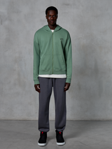 Alpinestars Essentials Ageless Zip Hoodie, hættetrøje med lynlås, kaktusgrøn, båret af en model med mørkegrå joggingbukser og sorte sneakers, med et lille sort Alpinestars-logo på brystet, afslappet pasform, casual streetwear.