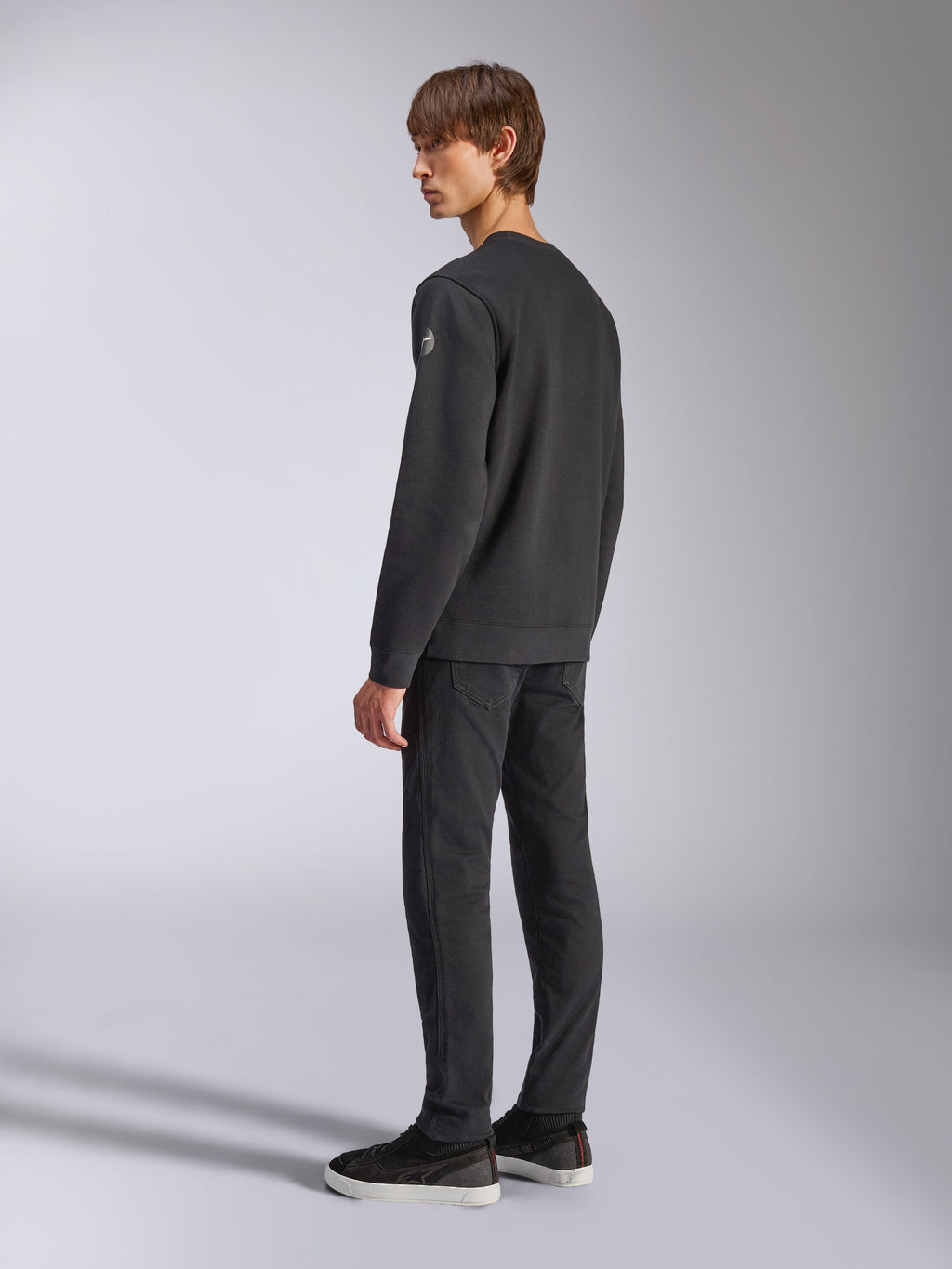Alpinestars Bettern Crew, Fleece Pullover, Black, male model shown from a back and side angle, featuring ribbed cuffs and hem with a small logo on the sleeve, casual motorsport-inspired streetwear