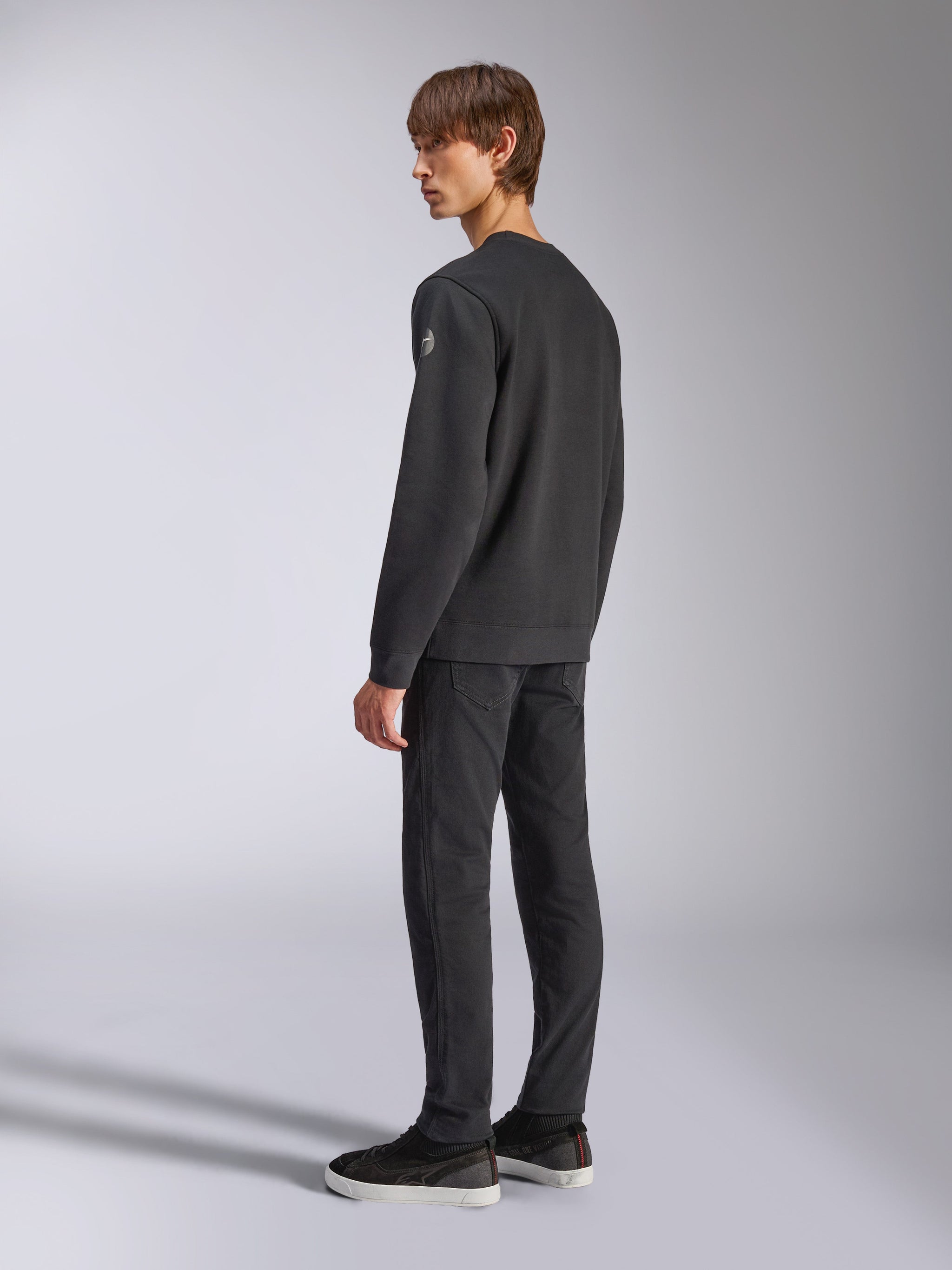 Alpinestars Bettern Crew, Fleece Pullover, Black, male model shown from a back and side angle, featuring ribbed cuffs and hem with a small logo on the sleeve, casual motorsport-inspired streetwear