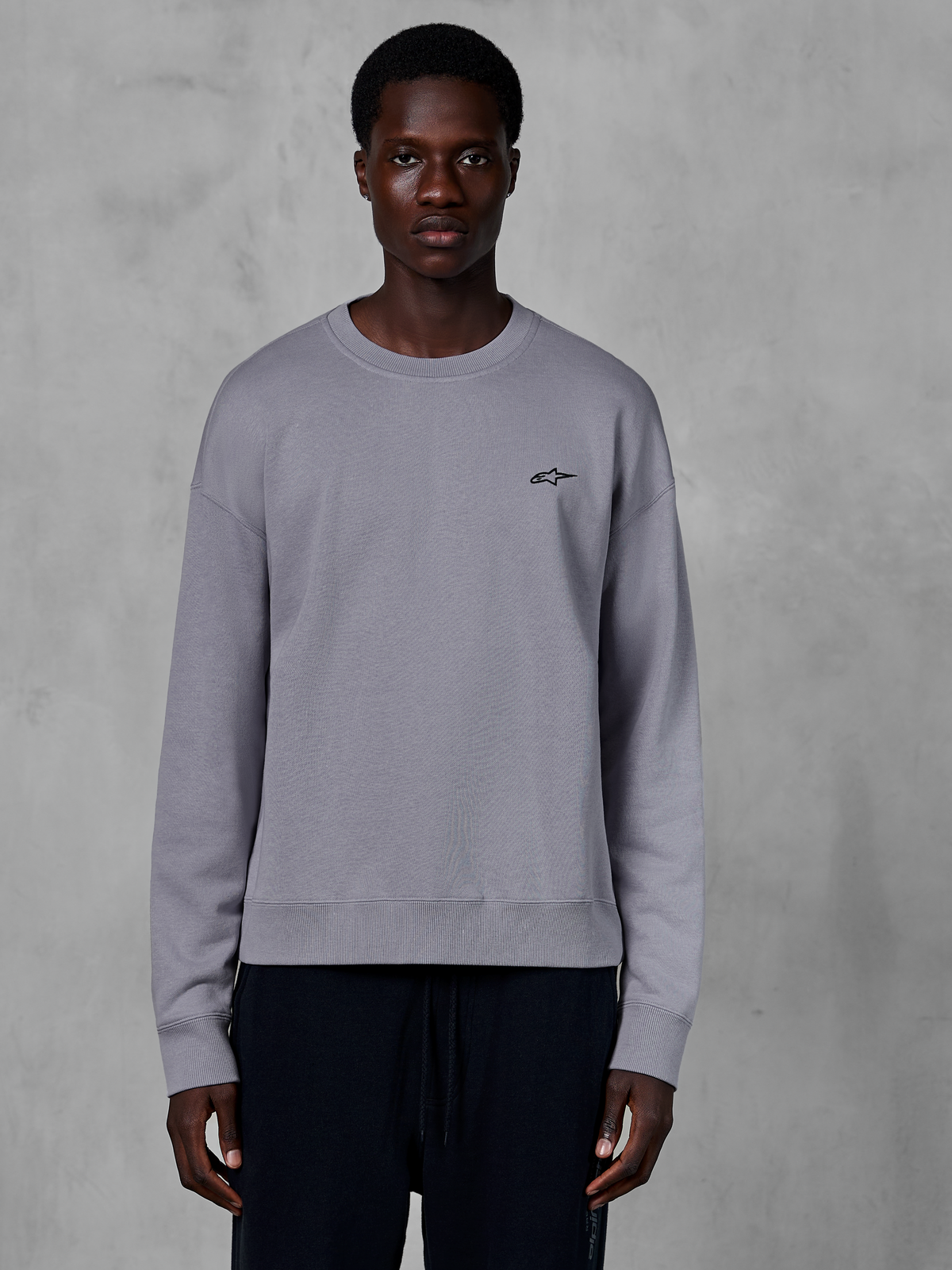 Alpinestars Essentials Ageless Crew, sølvfarvet crewneck sweatshirt båret af en model, med et lille sort stjernelogo på brystet, afslappet pasform med ribbede manchetter og kant, afslappet motorsport streetwear
