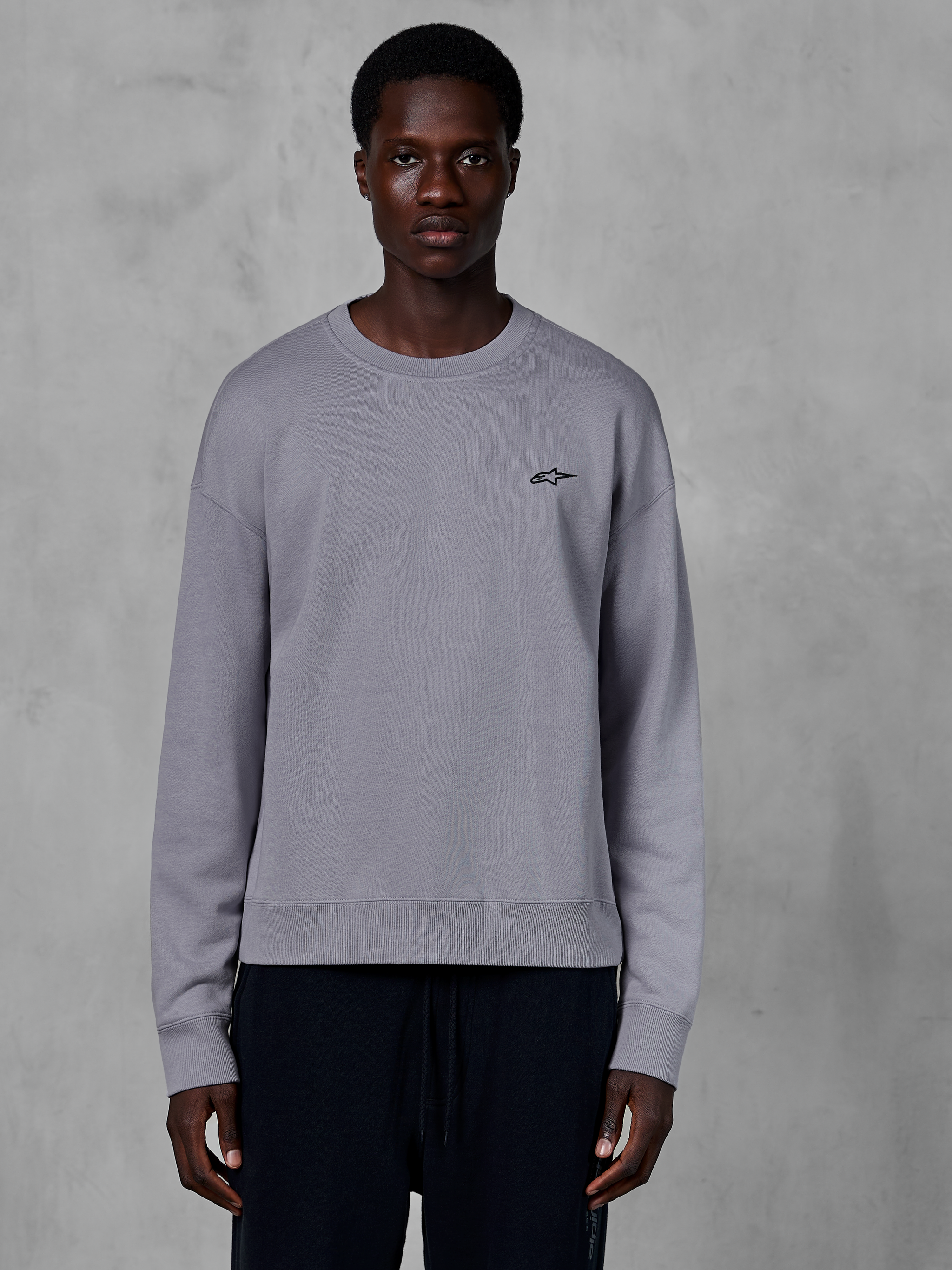 Alpinestars Essentials Ageless Crew, sølvfarvet crewneck sweatshirt båret af en model, med et lille sort stjernelogo på brystet, afslappet pasform med ribbede manchetter og kant, afslappet motorsport streetwear