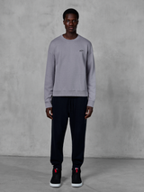 Alpinestars Essentials Ageless Crew, sølvfarvet sweatshirt med rund hals, båret af en model med sorte joggingbukser og sorte sneakers, med et lille sort Alpinestars-logo på brystet, afslappet motorsport-inspireret streetwear