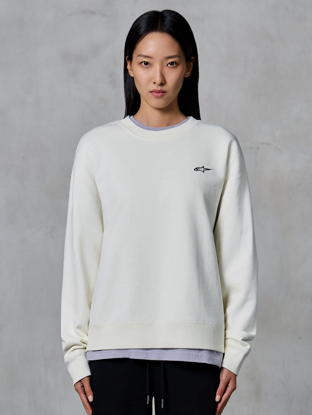 Alpinestars Essentials Ageless Crew, crewneck sweatshirt, off-white, med et lille sort Alpinestars-logo på brystet, afslappet livsstilstøj vist på en kvinde