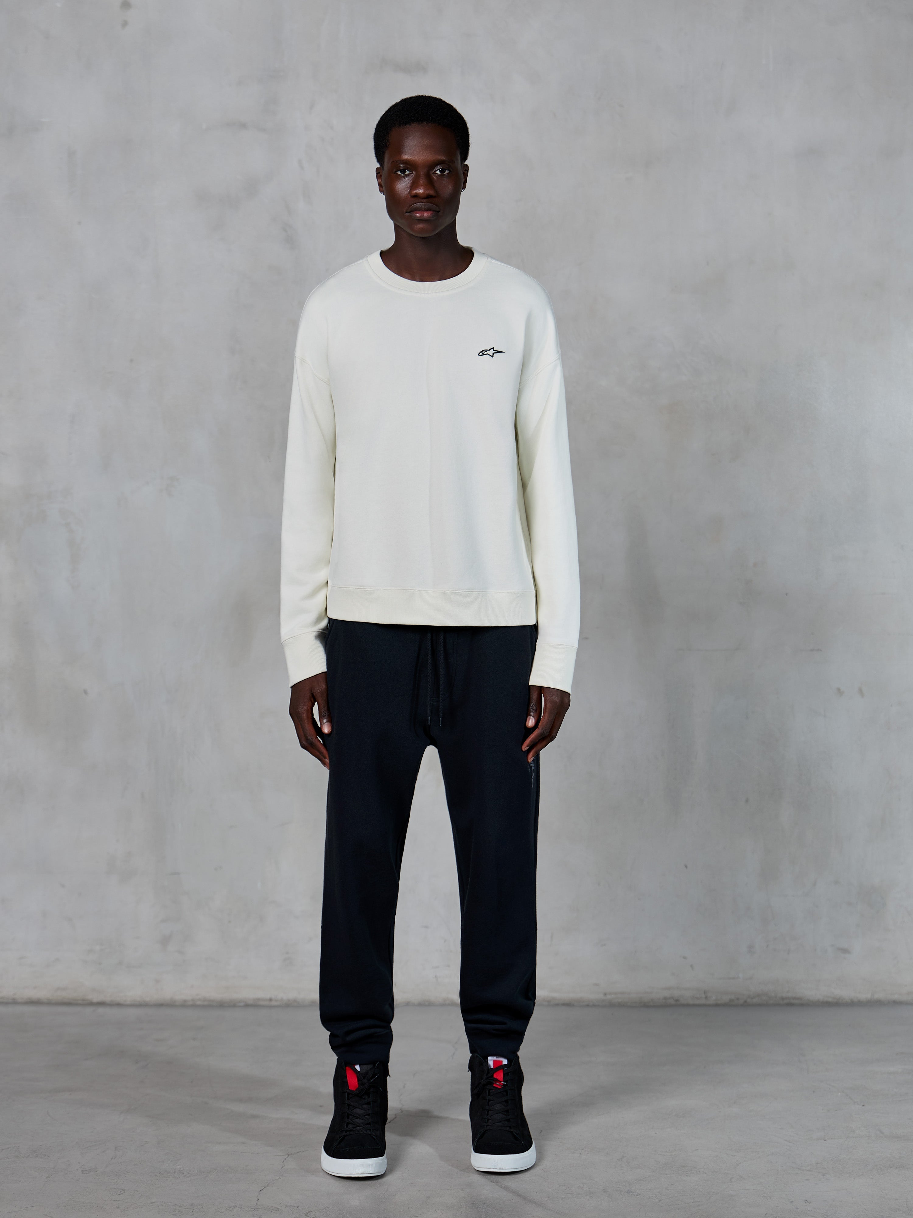 Alpinestars Essentials Ageless Crew, crewneck sweatshirt, off-white med lille sort stjerne-logo, båret af model med sorte joggingbukser, afslappet motorsport-inspireret streetwear