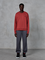 Alpinestars Essentials Ageless Crew, teglrød crewneck sweatshirt, båret med grå joggingbukser og sorte sneakers, med et lille sort logo på brystet, afslappet motorsport-inspireret streetwear