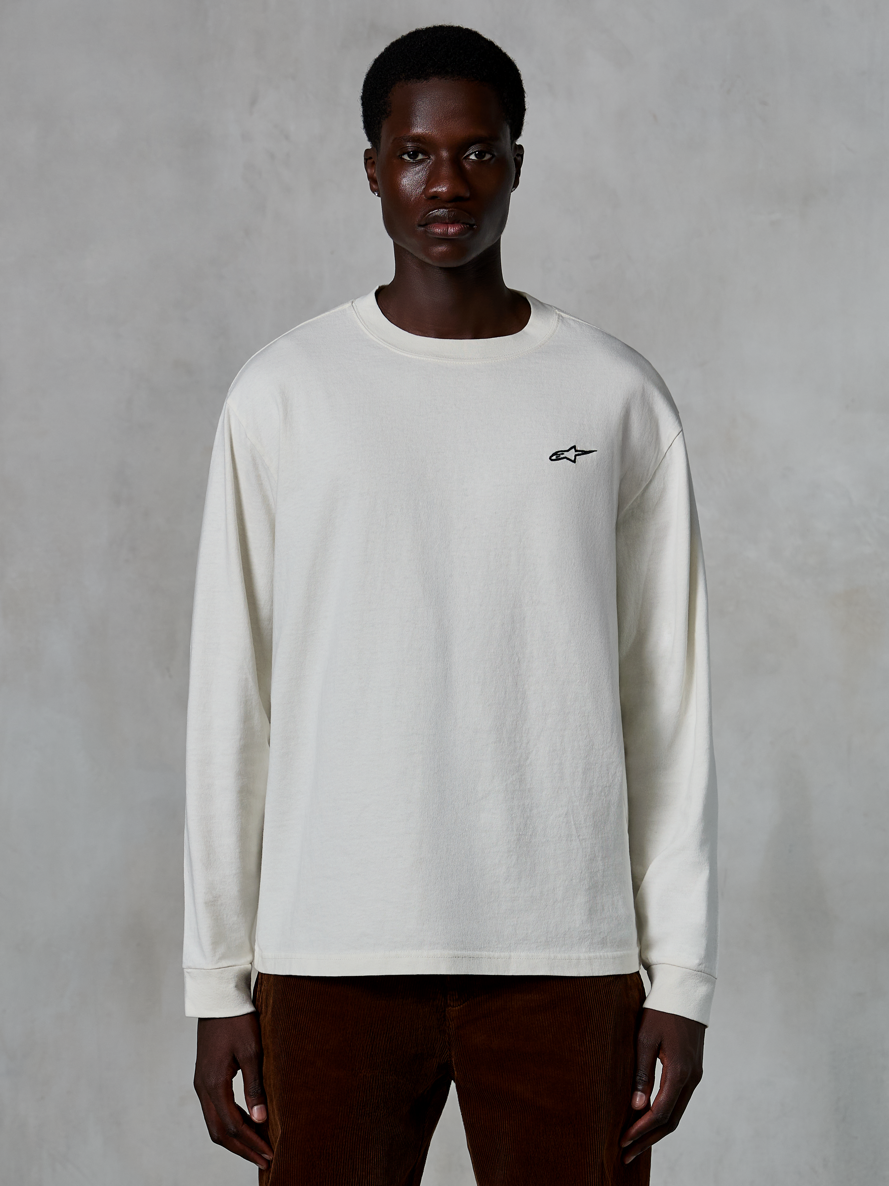 Alpinestars Essentials Ageless LS Tee, langærmet T-shirt, råhvid, lille sort stjernelogo på brystet, afslappet streetwear, afslappet pasform, båret af en model