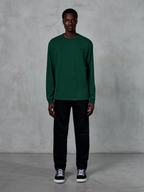 Alpinestars Essentials Ageless LS Tee, langærmet T-shirt, Pine Green, med et lille sort logo på brystet, båret af en model med sorte bukser og sneakers, afslappet streetwear-stil