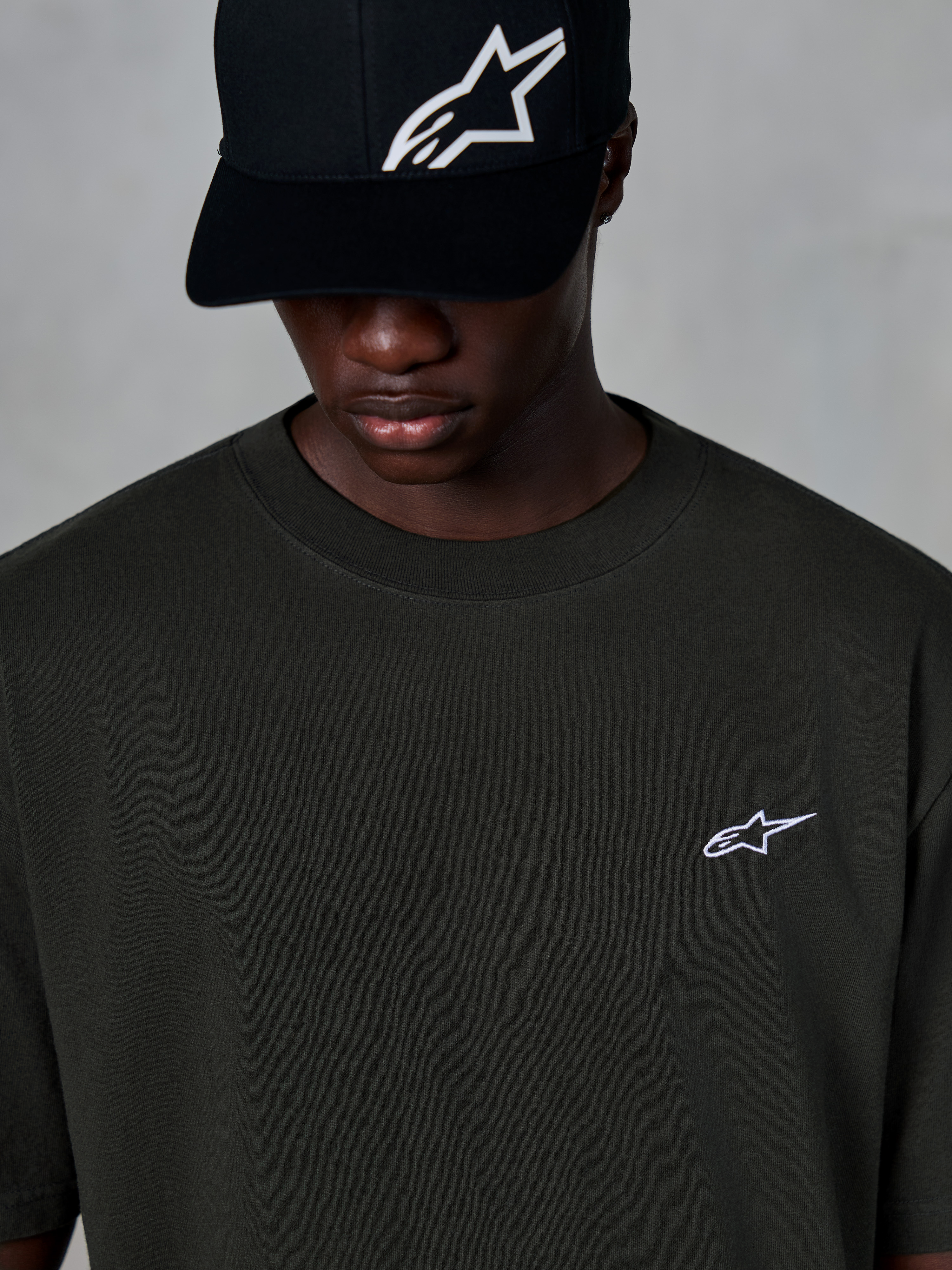 Alpinestars Essentials Ageless SS Tee, kortærmet t-shirt, Off Black, med et lille hvidt Alpinestars-logo på brystet, båret sammen med en sort baseball-kasket med logo, afslappet motorsport streetwear-stil
