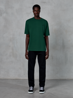 Alpinestars Essentials Ageless SS Tee, kortærmet T-shirt, Pine Green, med et diskret sort brystlogo, vist på en model med sorte bukser og sneakers, afslappet lifestyle-streetwear med en afslappet pasform