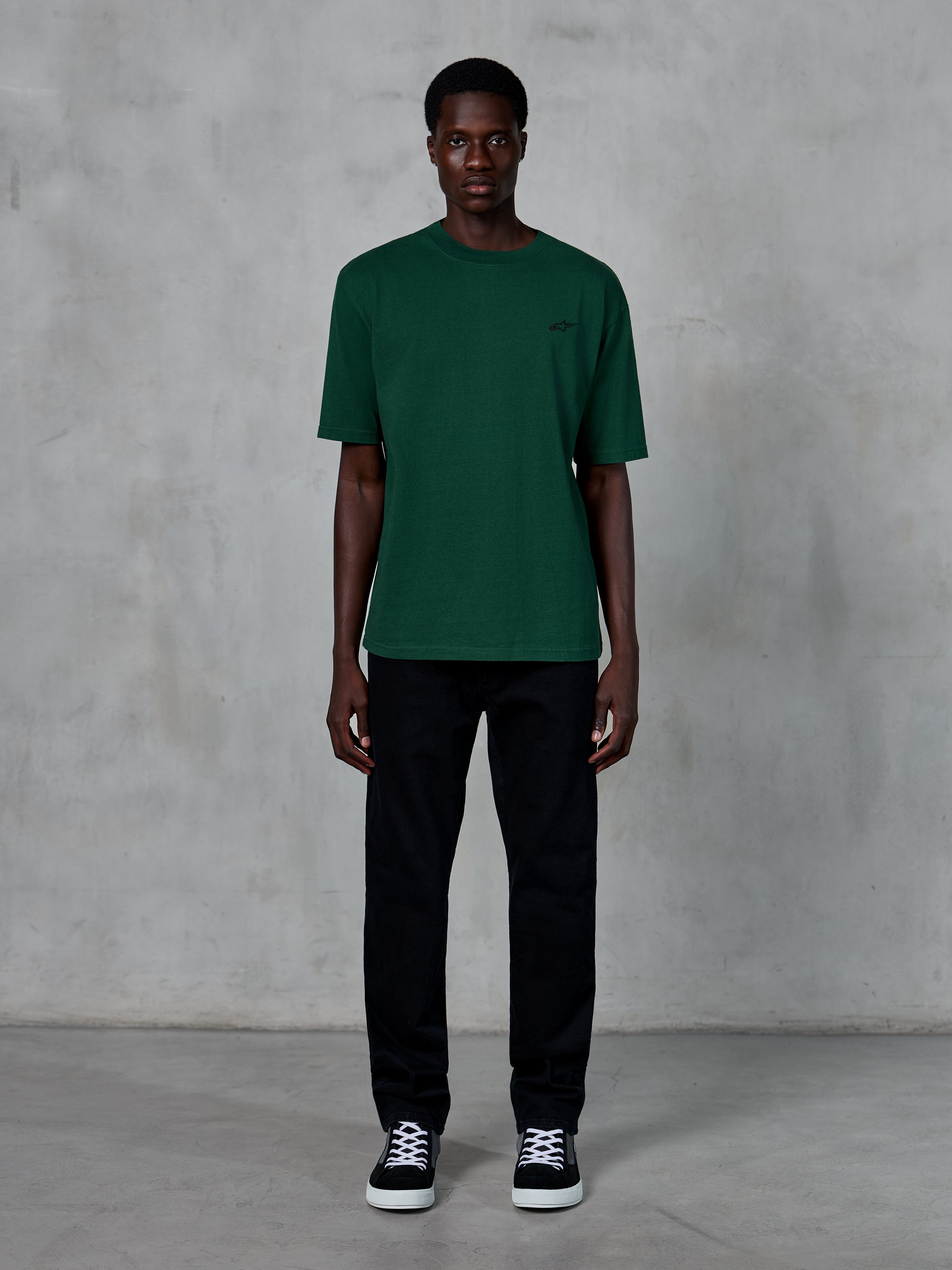 Alpinestars Essentials Ageless SS Tee, Short Sleeve T-Shirt, Pine Green, featuring a subtle black chest logo, worn by a model with black pants and sneakers, casual lifestyle streetwear with a relaxed fit