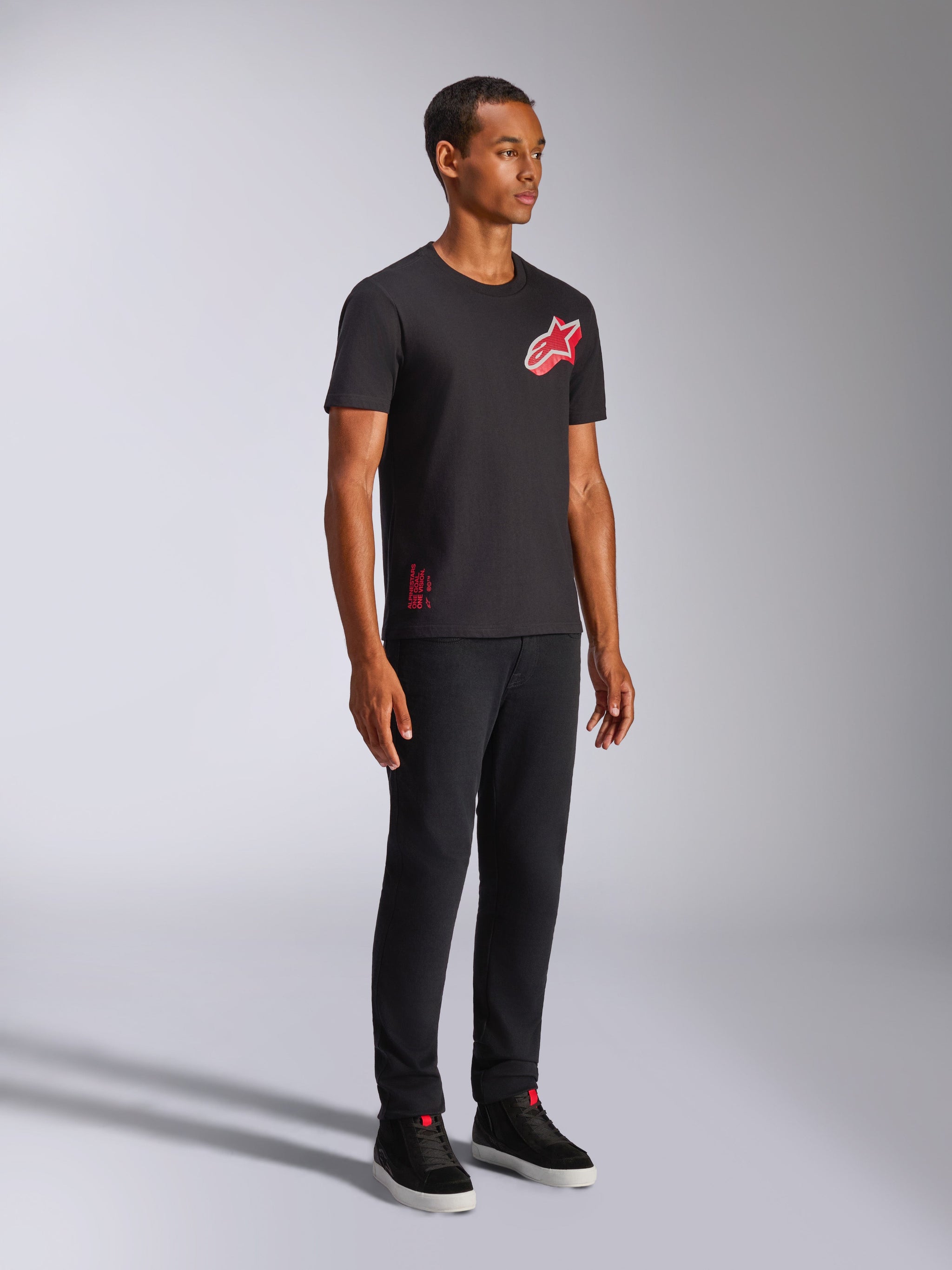 Alpinestars Shaded CSF t-shirt, kortærmet t-shirt, sort, rødt og hvidt skråtstillet gradient folie Astars-logo, casual motorsport-streetwear, fuldlængde billede af en model iført sorte bukser og sneakers