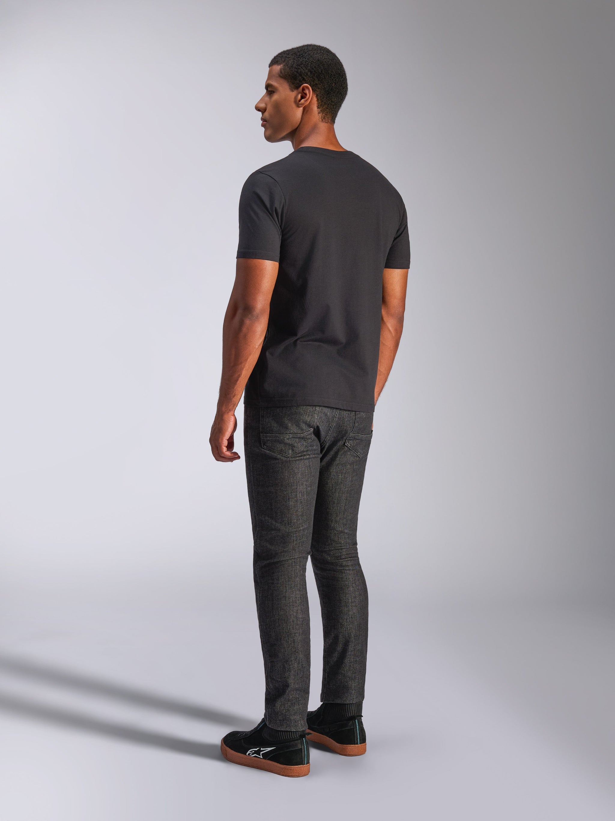 Alpinestars Tech Boot CSF Tee, kortærmet t-shirt, sort, set bagfra på model, kombineret med mørkegrå denimbukser og sorte sneakers, afslappet motorsport streetwear