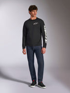 Alpinestars Trackside CSF Tee, langærmet t-shirt, sort og hvid, båret med mørkeblå jeans og sorte sneakers, med hvidt Ride 4.0-logo på brystet og Alpinestars-navnetræk på ærmet, afslappet motorsport-inspireret streetwear
