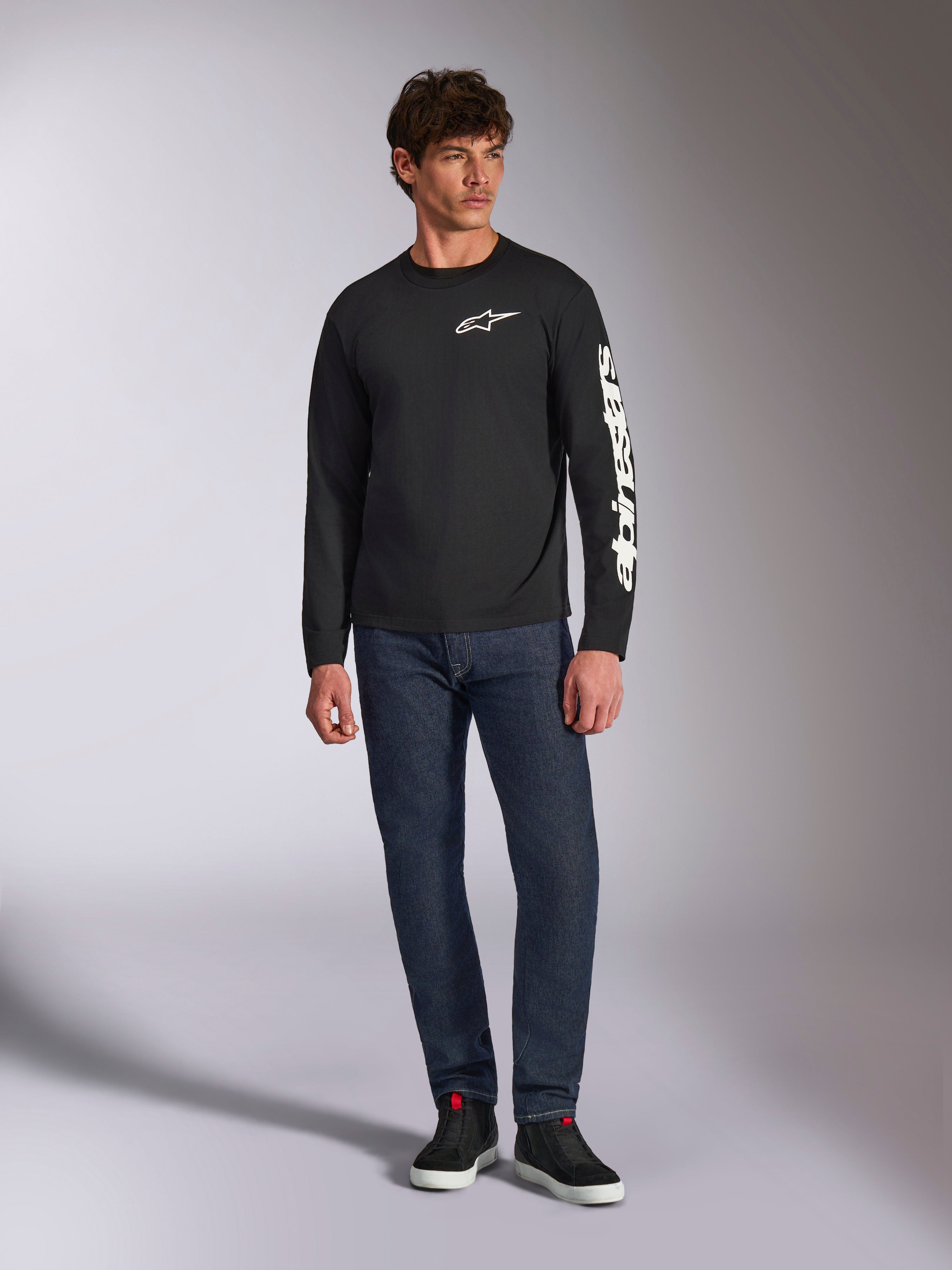 Alpinestars Trackside CSF Tee, langærmet t-shirt, sort og hvid, båret med mørkeblå jeans og sorte sneakers, med hvidt Ride 4.0-logo på brystet og Alpinestars-navnetræk på ærmet, afslappet motorsport-inspireret streetwear