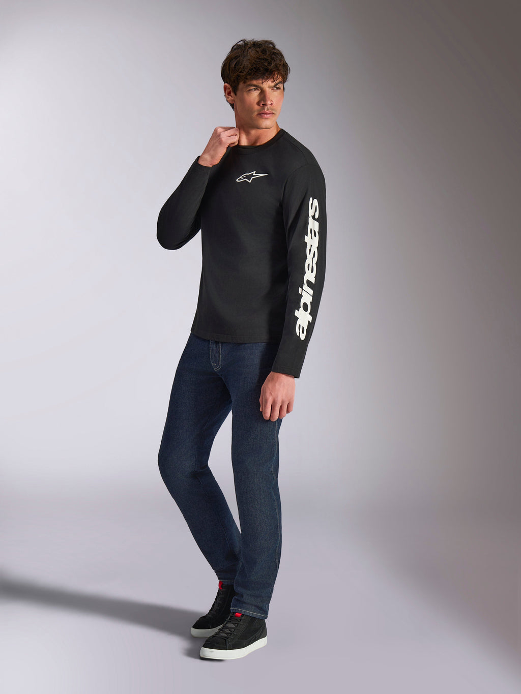Alpinestars Trackside CSF Tee, langærmet t-shirt, sort, hvid lodret Alpinestars-branding på ærmet og brystlogo, bæres af en mandlig model med mørkeblå jeans og sneakers, afslappet motorsport-streetwear