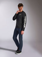 Alpinestars Trackside CSF Tee, langærmet t-shirt, sort, hvid lodret Alpinestars-branding på ærmet og brystlogo, bæres af en mandlig model med mørkeblå jeans og sneakers, afslappet motorsport-streetwear