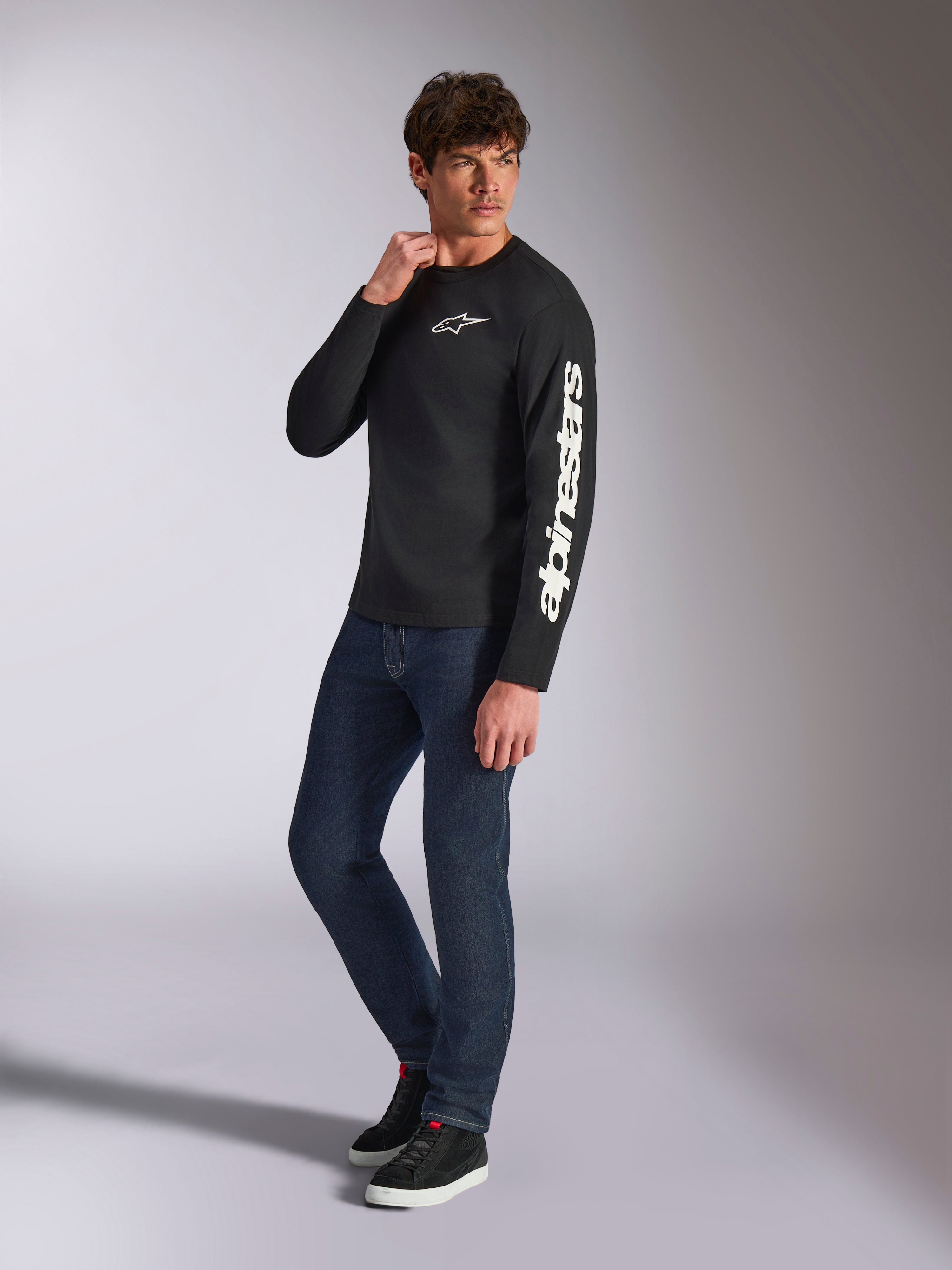 Alpinestars Trackside CSF Tee, langærmet t-shirt, sort, hvid lodret Alpinestars-branding på ærmet og brystlogo, bæres af en mandlig model med mørkeblå jeans og sneakers, afslappet motorsport-streetwear