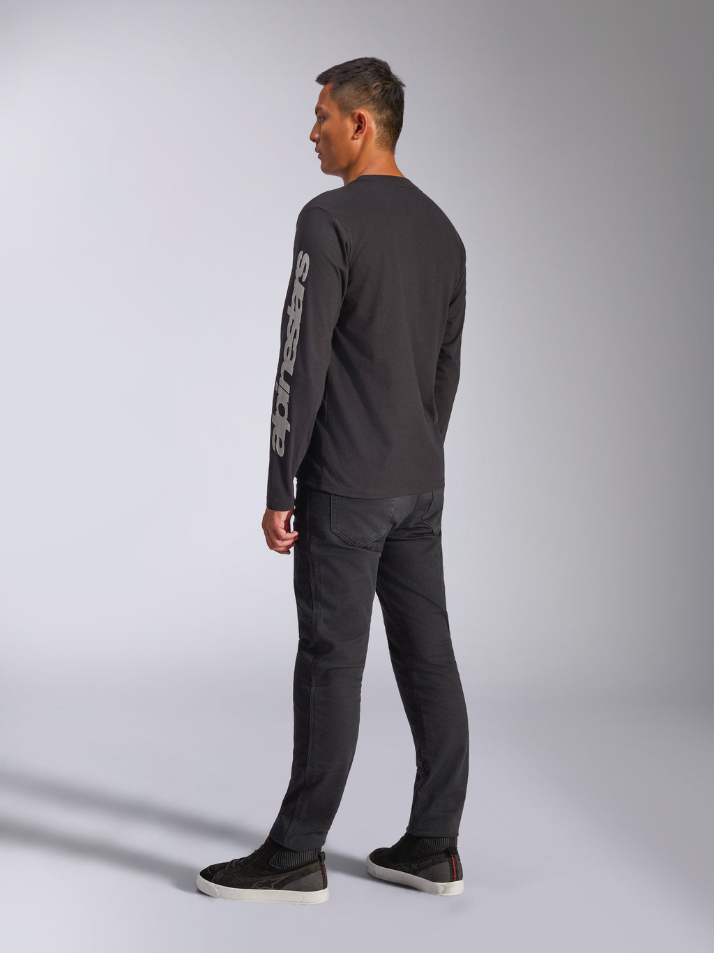 Alpinestars Trackside CSF Long Sleeve Tee, Black, featuring large grey Alpinestars logo on the left sleeve, worn by model with black pants and casual sneakers, motorsport-inspired casual streetwear.