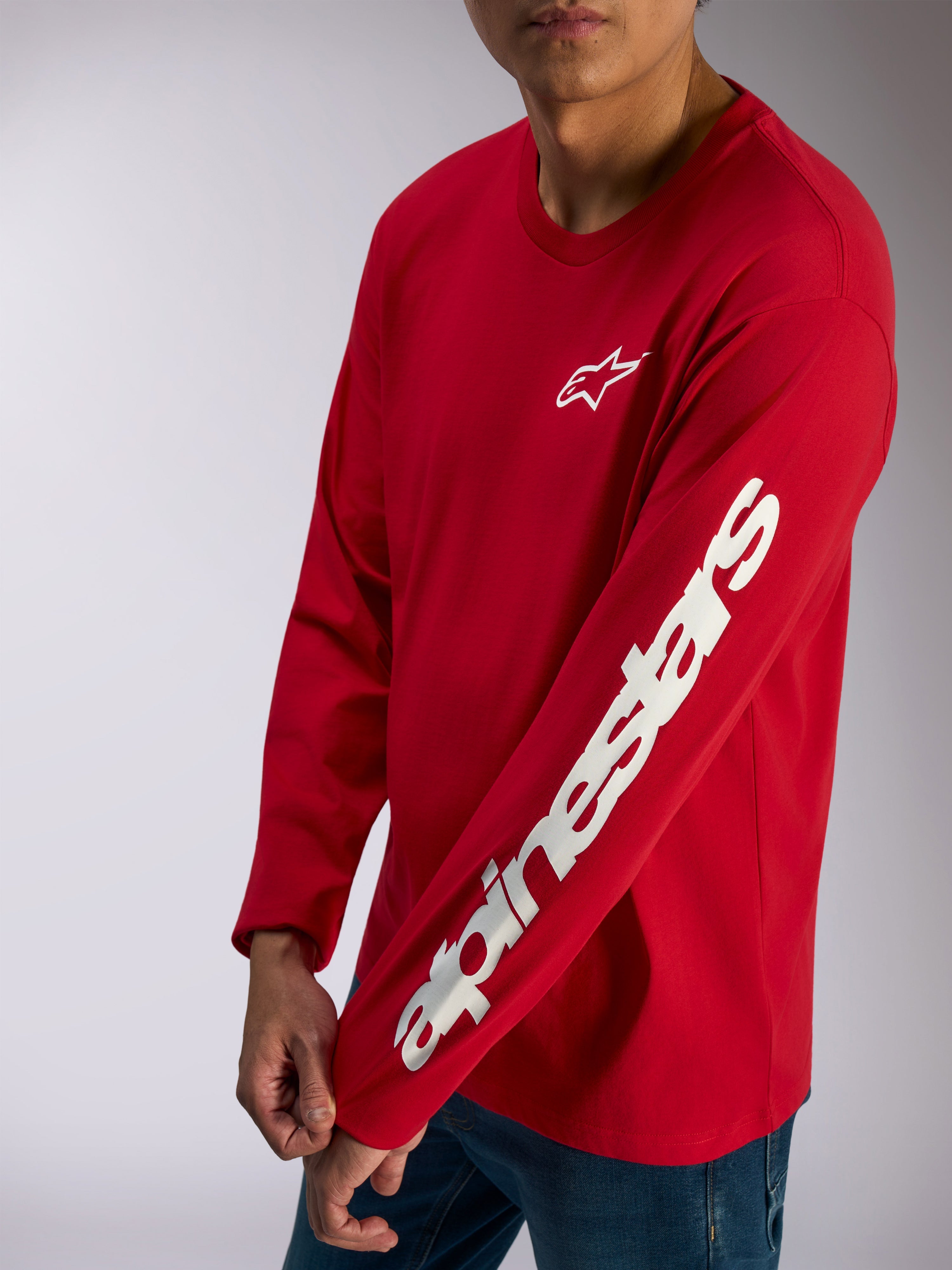 Alpinestars Trackside CSF Tee, langærmet t-shirt, rød, hvidt Alpinestars-logo på brystet og markant tekstlogo på ærmet, afslappet motorsport streetwear båret med blå jeans