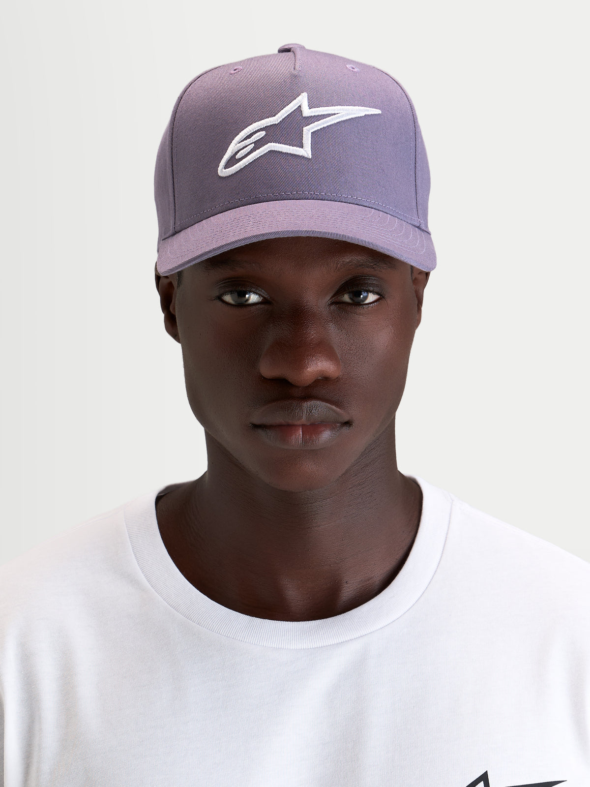 Alpinestars Ageless Snapback kasket, lilla og hvid sportswear-kasket med buet skygge, båret af model med det 3D-broderede Astars-logo foran