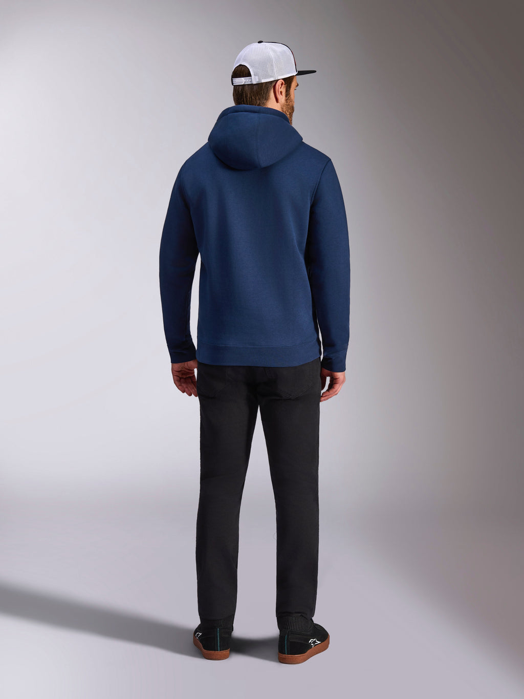 Alpinestars Frontal hættetrøje, marineblå, set bagfra af mand iført afslappet pullover-fleecehættetrøje med ribmanchetter og ribkant, kombineret med sorte bukser og en hvid mesh-kasket, motorsport-inspireret streetwear