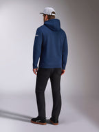 Alpinestars Frontal Hoodie, mørkeblå pullover fleece hættetrøje set bagfra, hvidt tekstlogo på ærmet, sorte bukser og hvid mesh trucker kasket, afslappet motorsport-inspireret streetwear