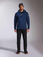 Mandlig model iført Alpinestars Frontal Hoodie i Navy, pullover fleece med hvidt Astars-logo på brystet og tekstlogo på ærmet, kængurulomme og hætte med snøre, kombineret med sorte bukser og kasket med logo, afslappet motorsport-streetwear