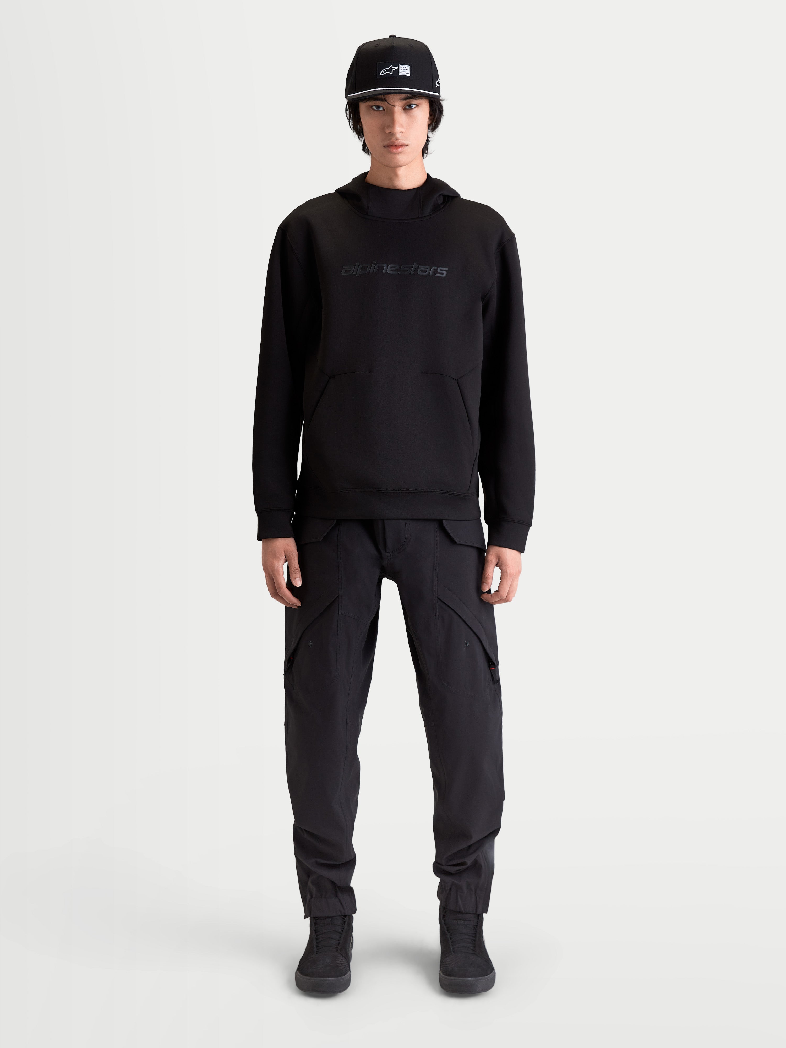 Alpinestars Datrix hættetrøje, premium sportstøj pullover til herre, sort, med tonal HD Alpinestars branding, tri-blend dobbeltsidet fleece og lomme med indsnitsdetalje, vist på model for en motorsport-inspireret hverdagsstil.