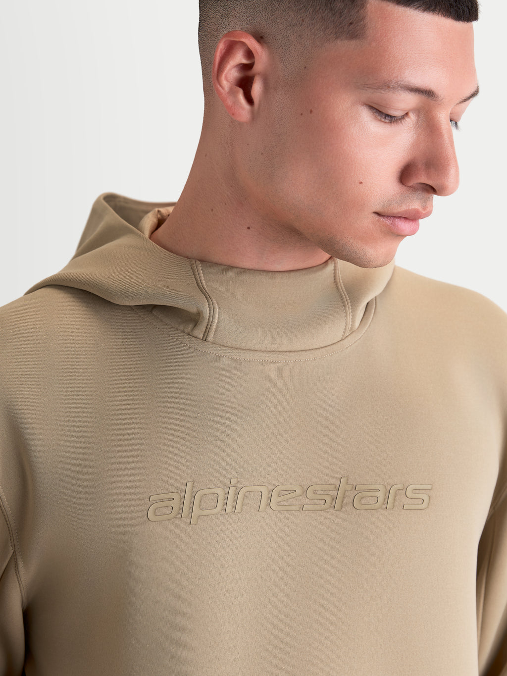 Alpinestars Datrix hættetrøje, sportswear pullover til mænd og kvinder, brun, med tonalt Alpinestars-logo og mesh-foret hætte, nærbillede af model der viser premium fleece-konstruktionen.