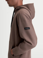 Alpinestars Camino Textured Oversized hættetrøje, brun, tekstureret strikket twill-fleece, sidevisning på model med vævet Alpinestars-label på ærmet, afslappet sportswear.