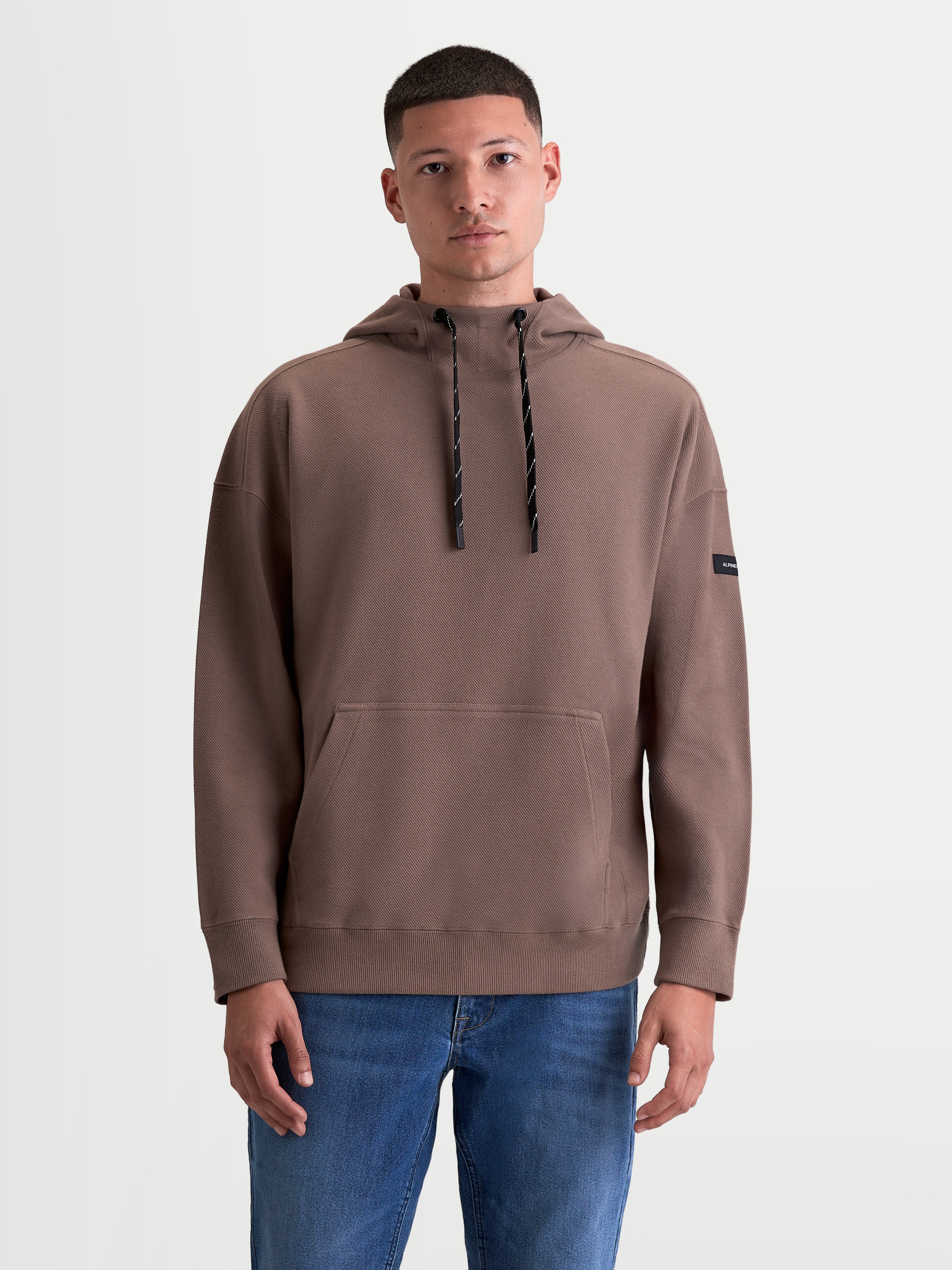 Alpinestars Camino Textured Oversized Hættetrøje til herrer, brun sportswear pullover i struktureret strikket twill-fleece med høj krave, kængurulomme og snoretræk i hætten, motorsport-inspireret livsstilstøj.