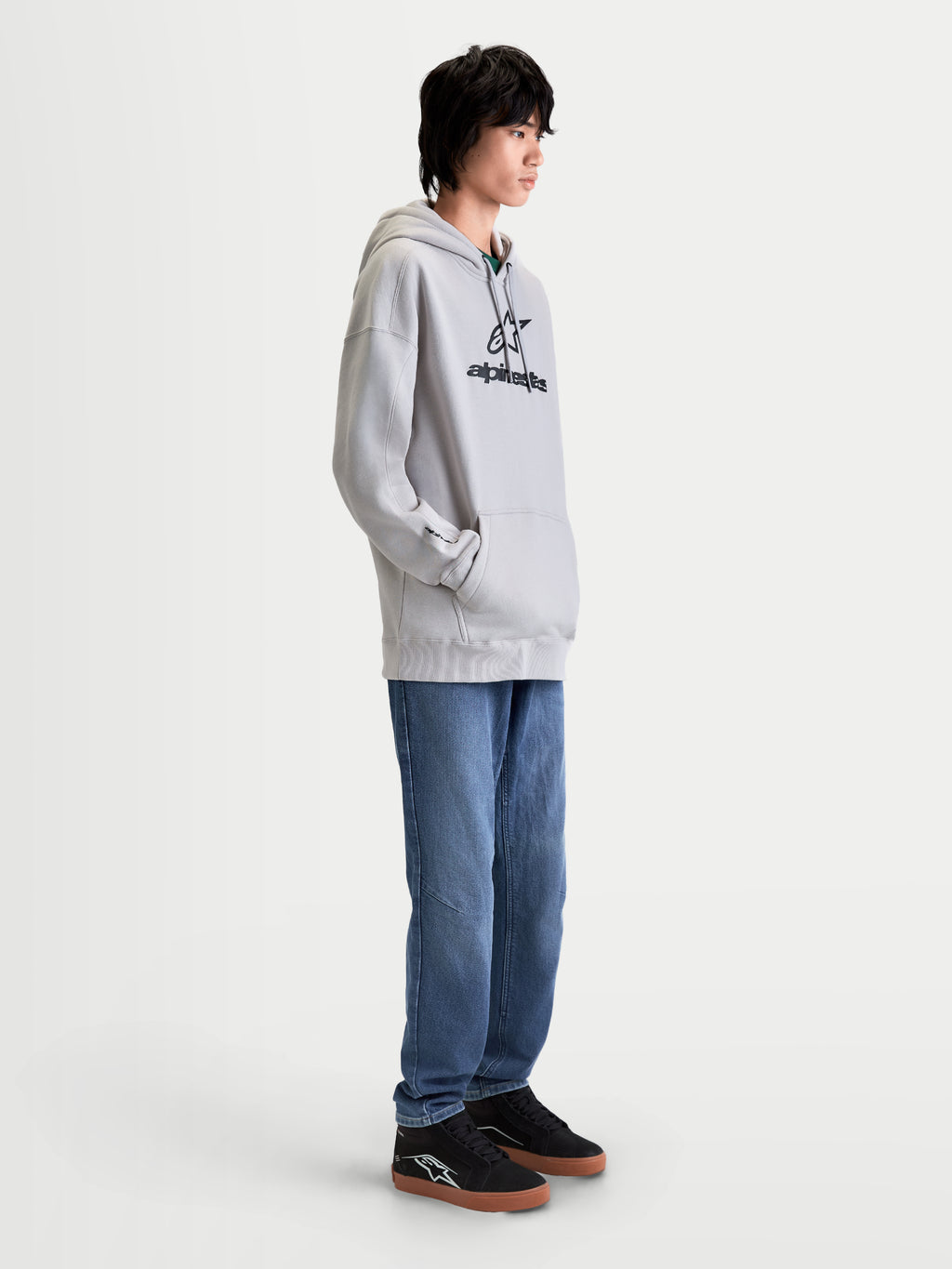 Alpinestars Prelude Oversized Hættetrøje, afslappet herremodel i cementgrå med sort puff-print-logo på brystet, komfortabel fleece-pullover med oversized pasform, kængurulomme og selvforet hætte, vist på model i profil.