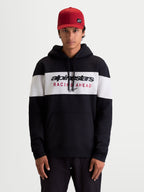 Alpinestars Cubic hættetrøje, herre sportswear pullover fleece i sort og hvidt farveblokeret design, Alpinestars Racing Ahead-logo på brystet, kængurulomme og snøre i hætten, afslappet livsstilstøj set på model med rød kasket.