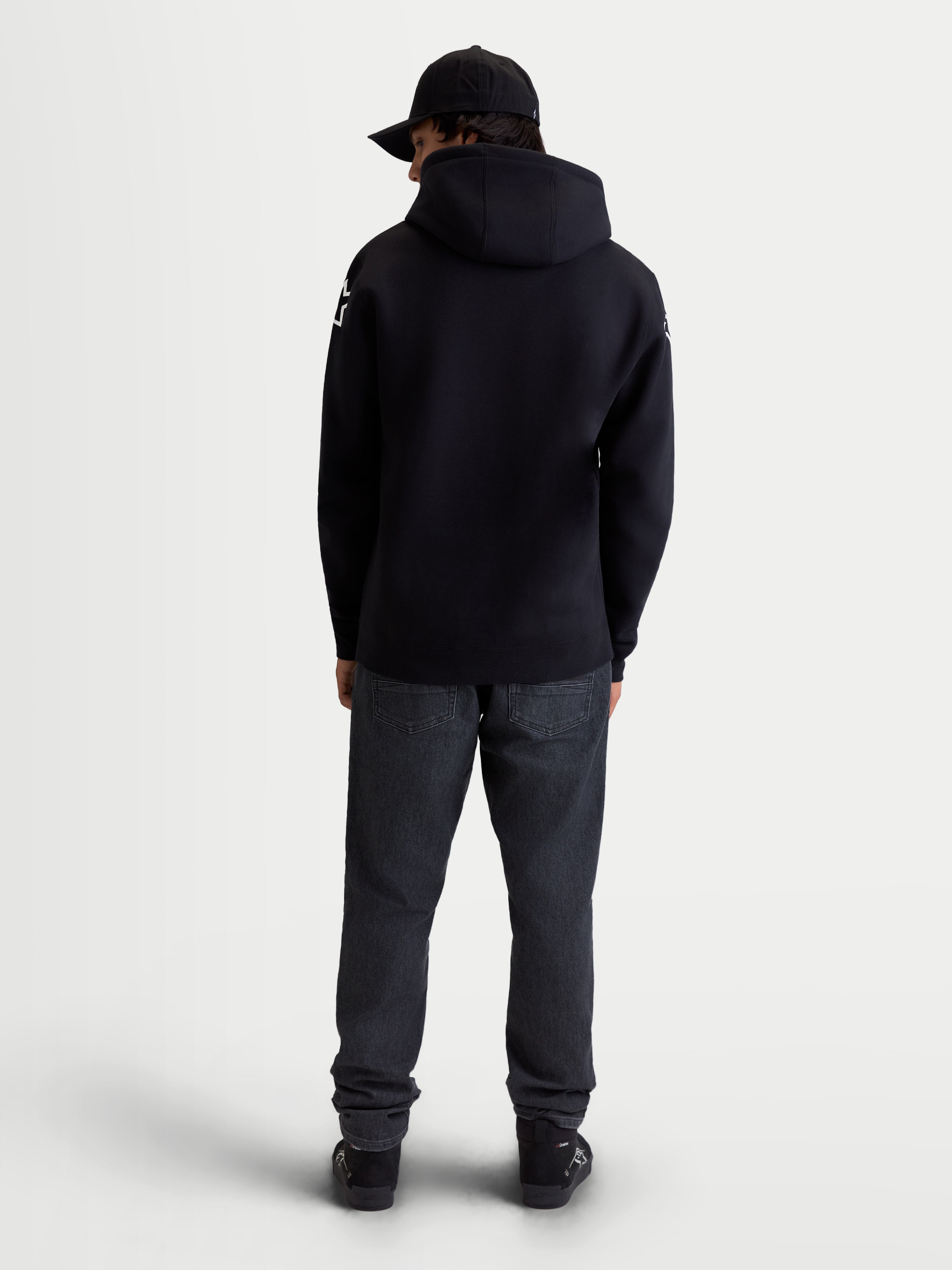 Alpinestars Velocifier hættetrøje, herrehættetrøje i fleece til sportstøj, sort, blanding af bomuld og genanvendt polyester, set bagfra på model med hætte og hvide Alpinestars-logoer på skuldrene.