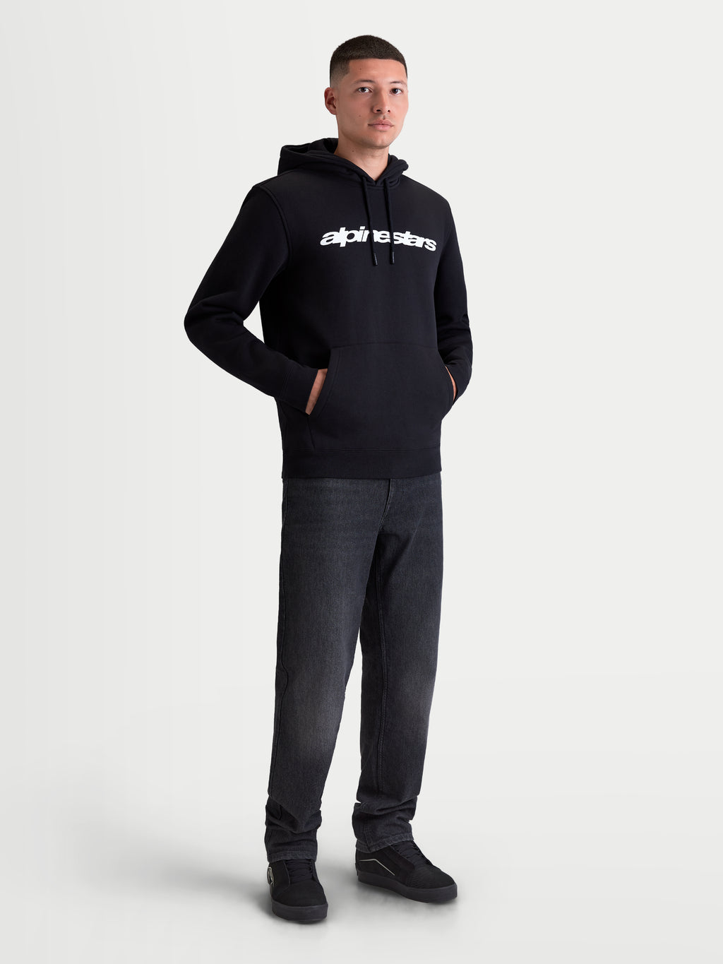 Alpinestars Race Wordmark Hoodie, Men's Sportswear Pullover Fleece, Black and White, featuring a bold white linear chest logo, self-lined hood with drawstrings, and a front pouch pocket. Constructed from a comfortable cotton and recycled polyester blend for everyday casual wear, shown on model.