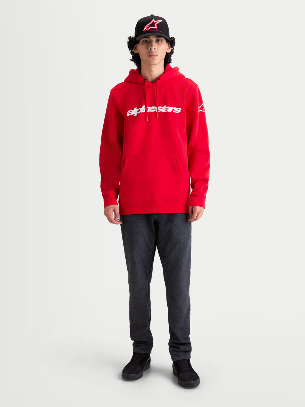 Alpinestars Race Wordmark hættetrøje, rød fleecehættetrøje med hvidt logoprint på brystet, kængurolomme og justerbar hætte med snøre, båret af en model for et afslappet motorsport-look.