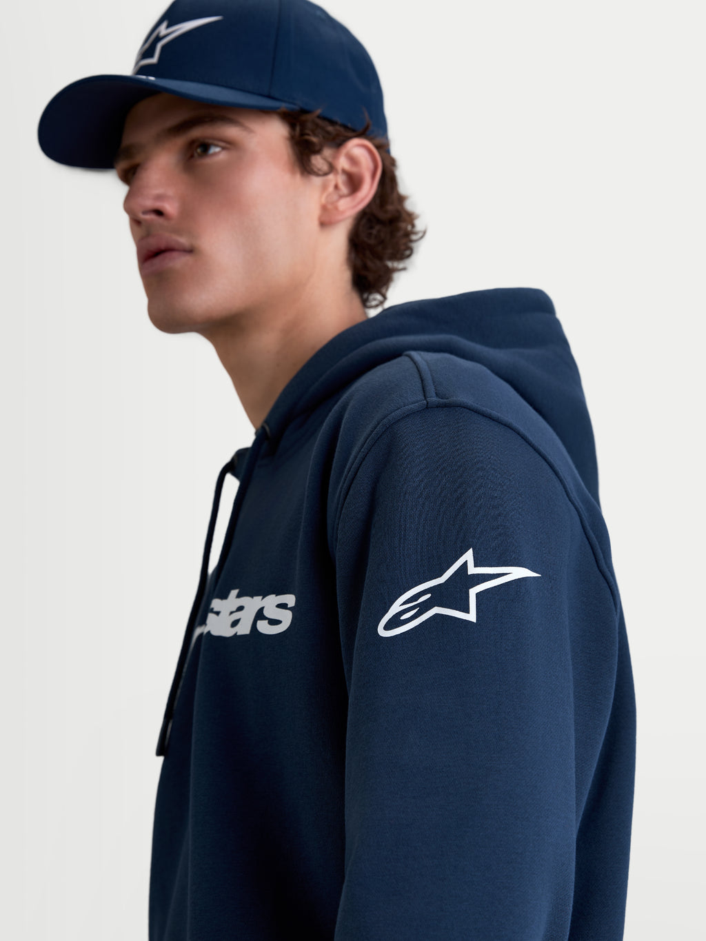 Alpinestars Race Wordmark hættetrøje, herre-fleecehættetrøje i mørkeblå og hvid med hvidt Ageless-logo på ærmet og Race Wordmark-grafik på brystet, livsstilsbillede af model i profil.