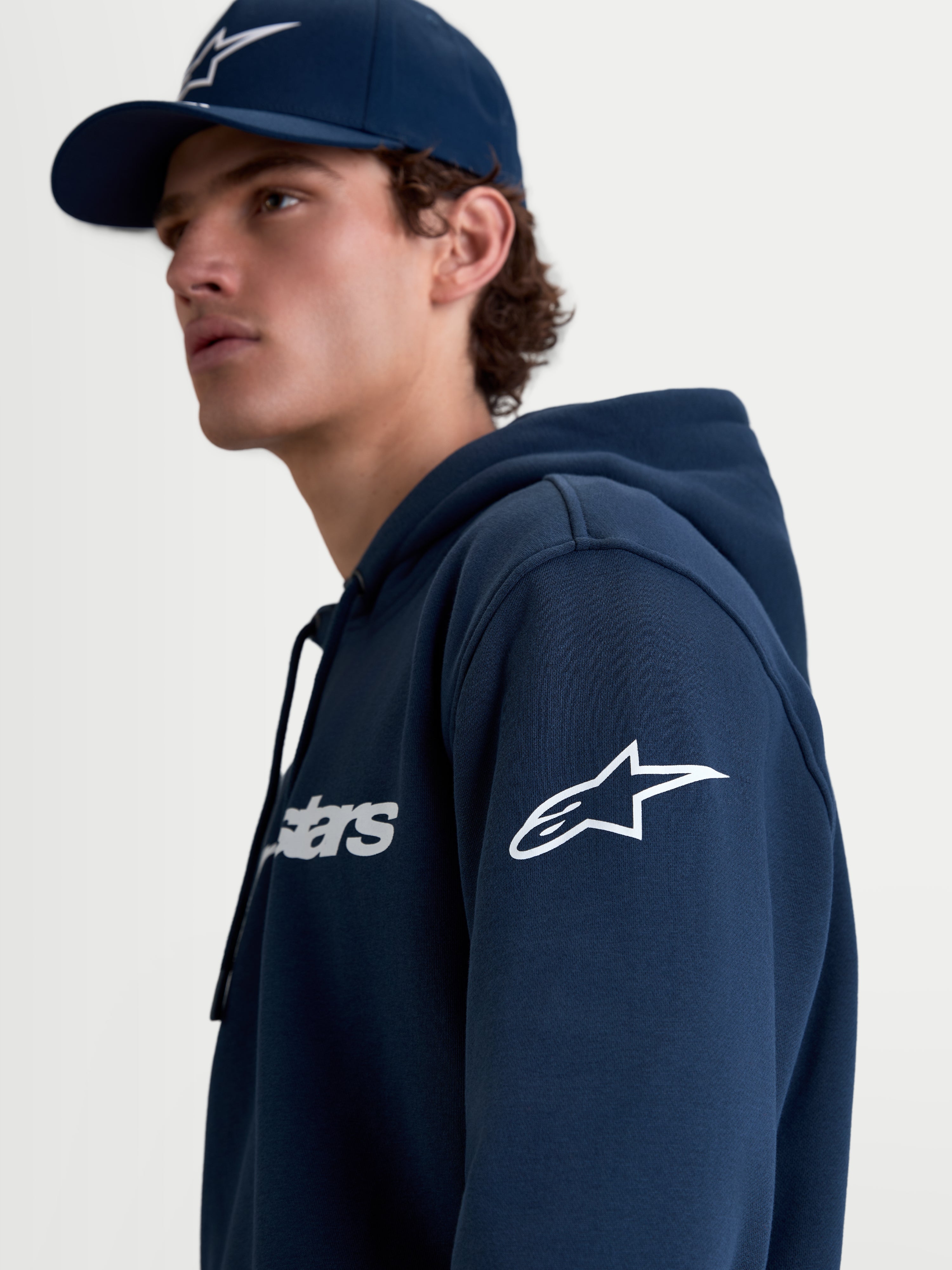 Alpinestars Race Wordmark hættetrøje, herre-fleecehættetrøje i mørkeblå og hvid med hvidt Ageless-logo på ærmet og Race Wordmark-grafik på brystet, livsstilsbillede af model i profil.