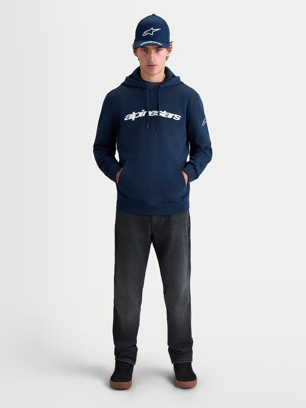 Alpinestars Race Wordmark hættetrøje, sportswear fleece pullover i mørkeblå og hvid, med markant tekstgrafik på brystet og Ageless-logo på ærmet, livsstilsbillede med model for et afslappet motorsportsinspireret look.