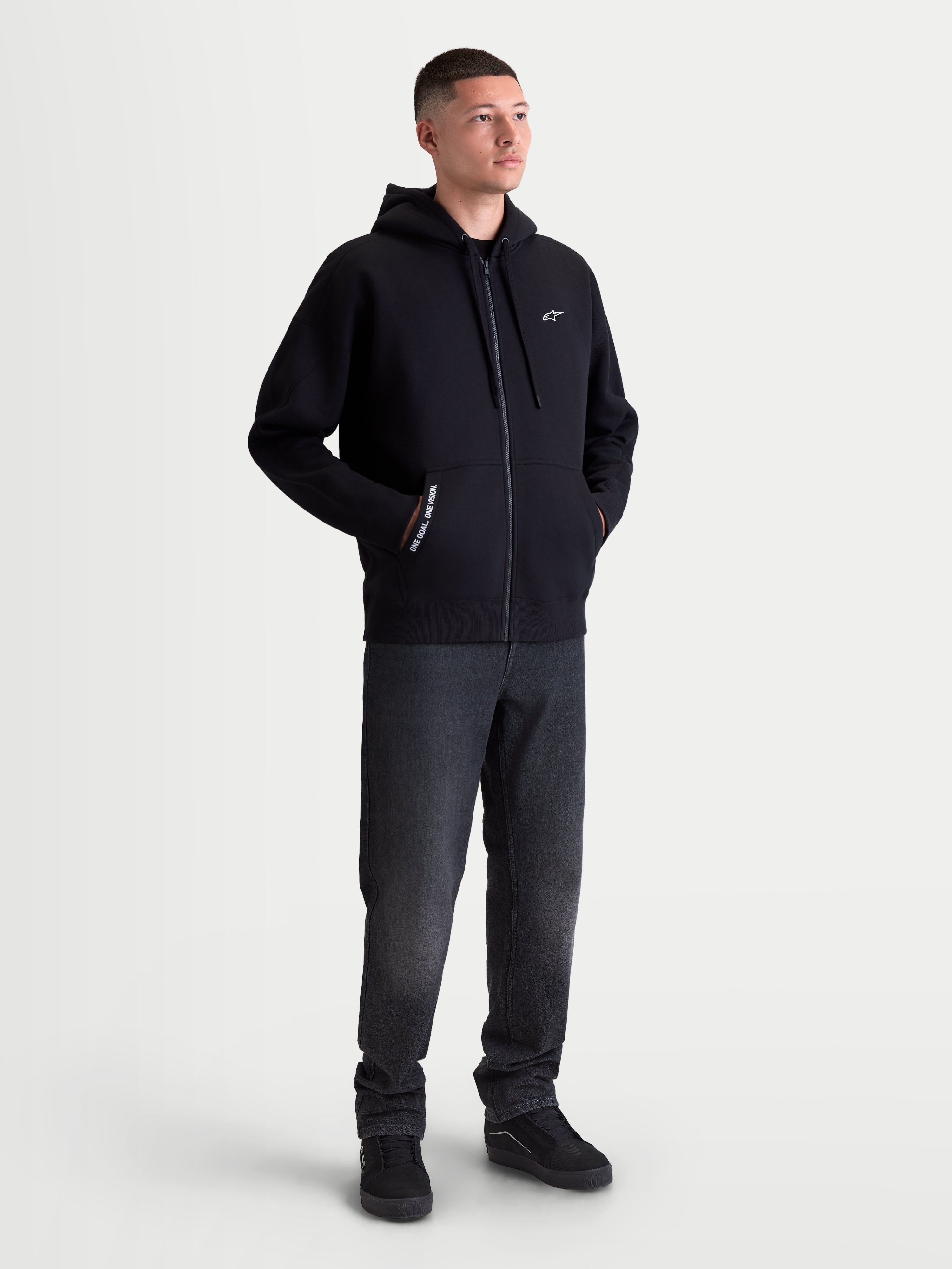 Alpinestars Pioneer Oversized Hættetrøje, sort hættetrøje med lynlås i fleece til herre og dame, afslappet oversized pasform, Vislon-lynlås, kængurulomme med 'ONE GOAL. ONE VISION.' tekst og hvidt Astars-logo på brystet, bomuldsblanding til hverdagsbrug.