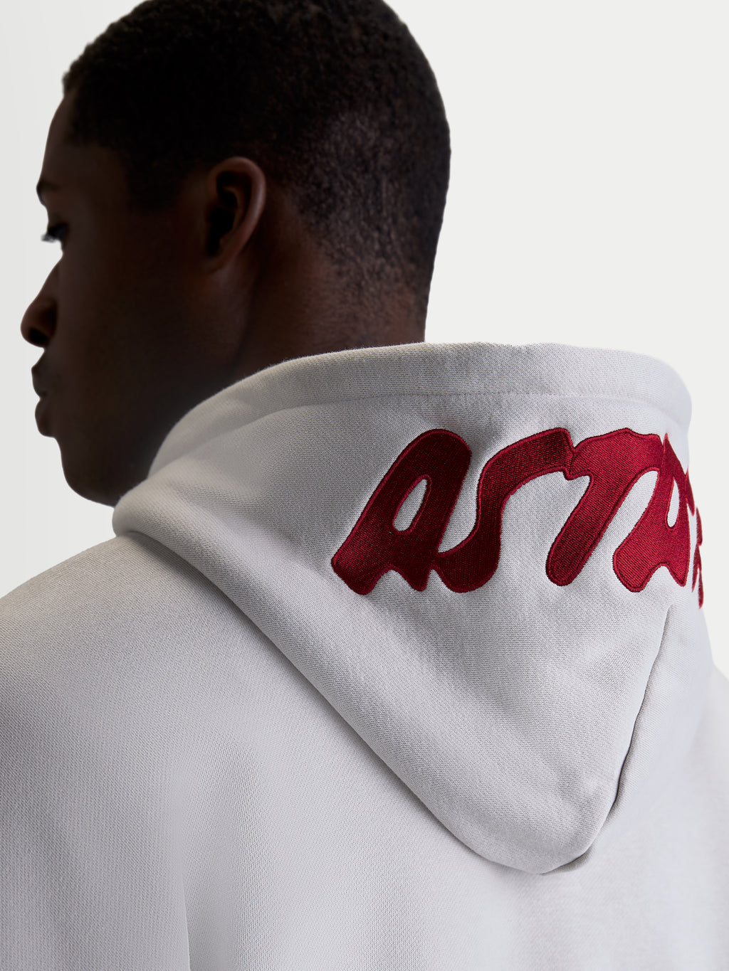 Alpinestars Pioneer Oversized hættetrøje, afslappet sportswear fleece, unisex, cementgrå med rødt broderet logo på hætten, set bagfra på model der fremhæver den oversized pasform.