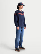 Alpinestars Velocifier CSF T-shirt, langærmet herre-trøje i marineblå og orange med buet Astars-grafik og skulderlogoer, fremstillet af bomuld og genanvendt polyester, vist på model til casual lifestyle.