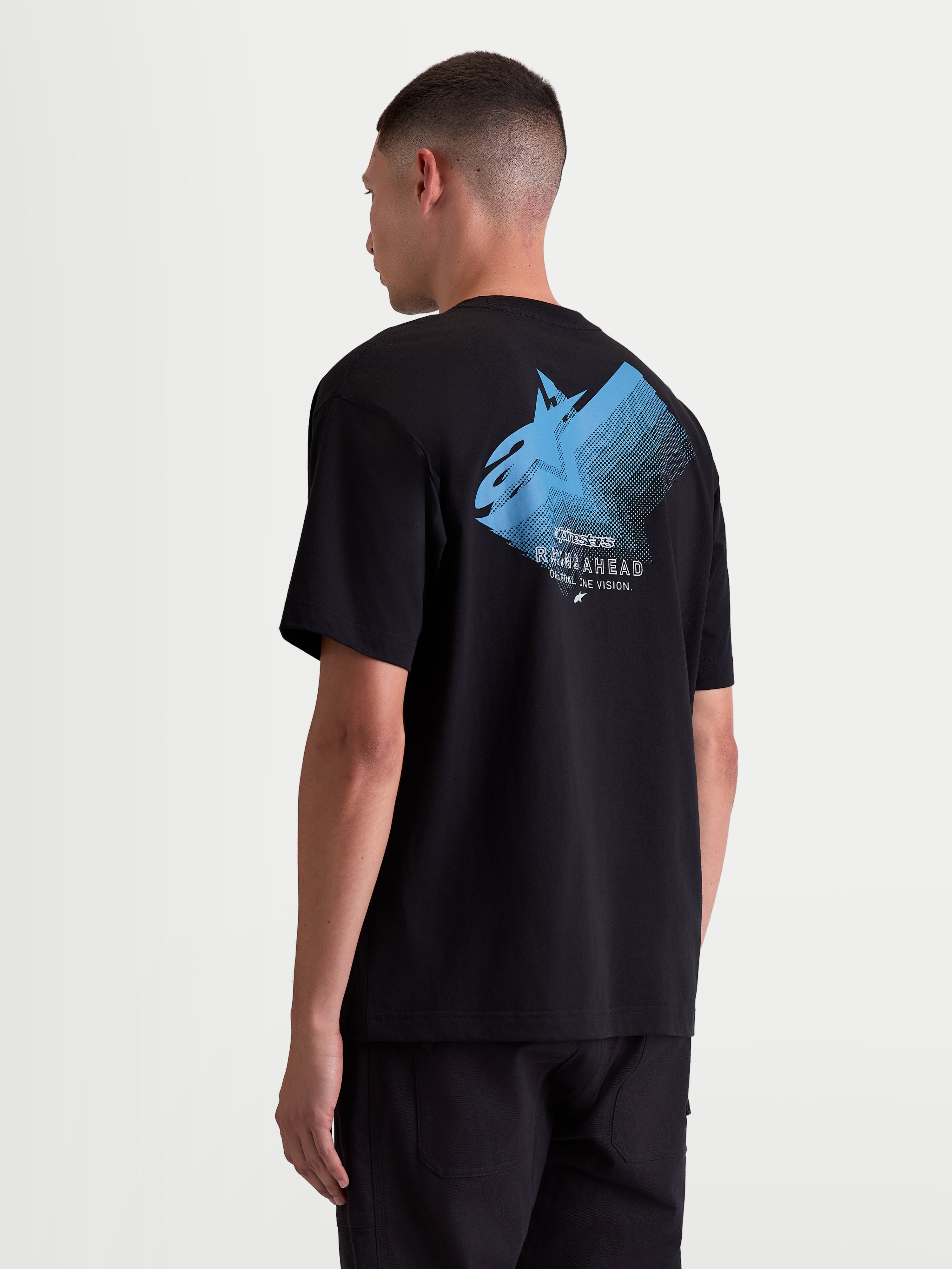 Alpinestars Ghost Oversized CSF Tee, Men’s Short Sleeve Sportswear T-shirt, Black with Blue graphic. Back view on model showing a large Astars fade logo with 'Racing Ahead' and 'One Goal. One Vision.' text. Relaxed oversized fit in a soft cotton-poly blend for casual off-bike wear.