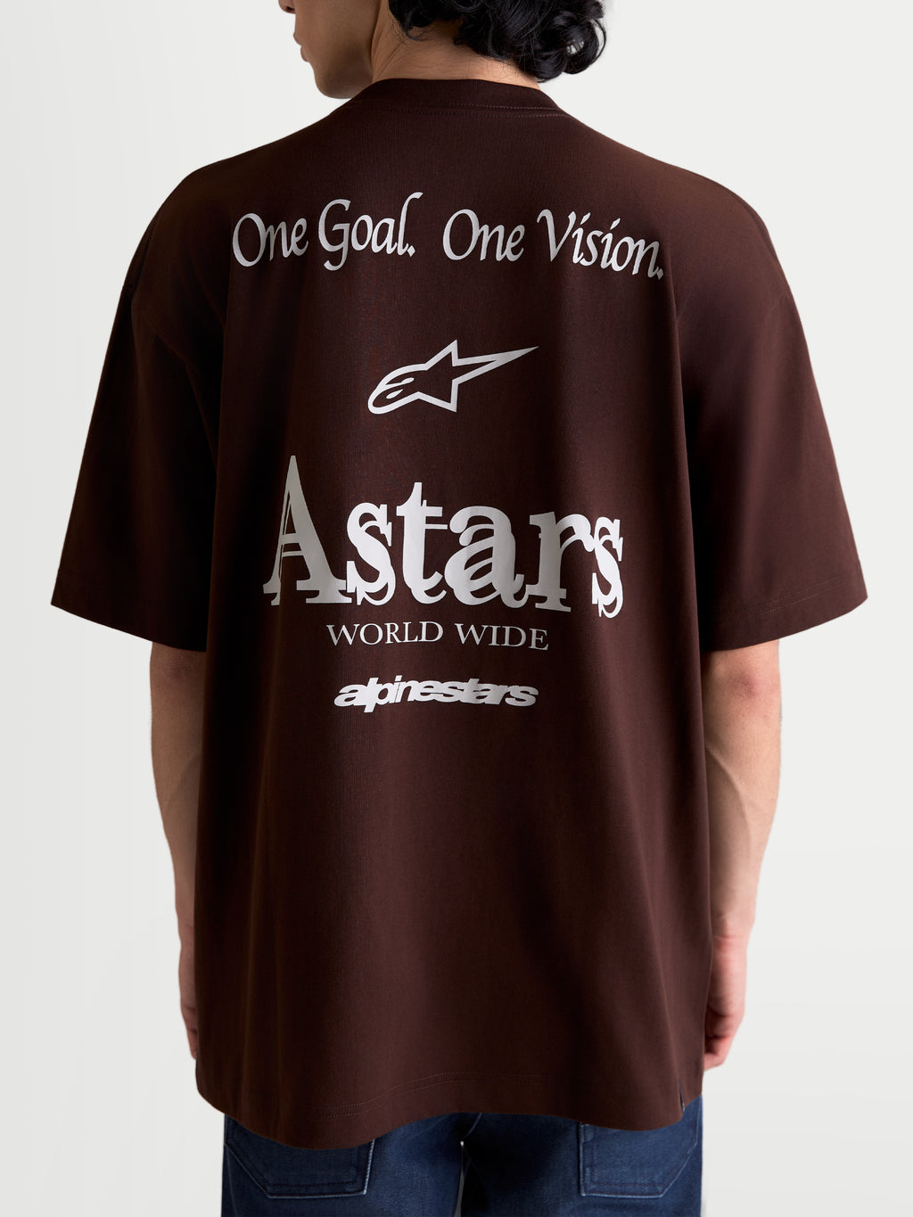 Alpinestars Post Oversized CSF T-shirt, brun kortærmet T-shirt set bagfra på model med hvid 'One Goal. One Vision.' og 'Astars World Wide' grafik, oversized pasform i bomulds-polyesterblanding, afslappet motorsport sportstøj