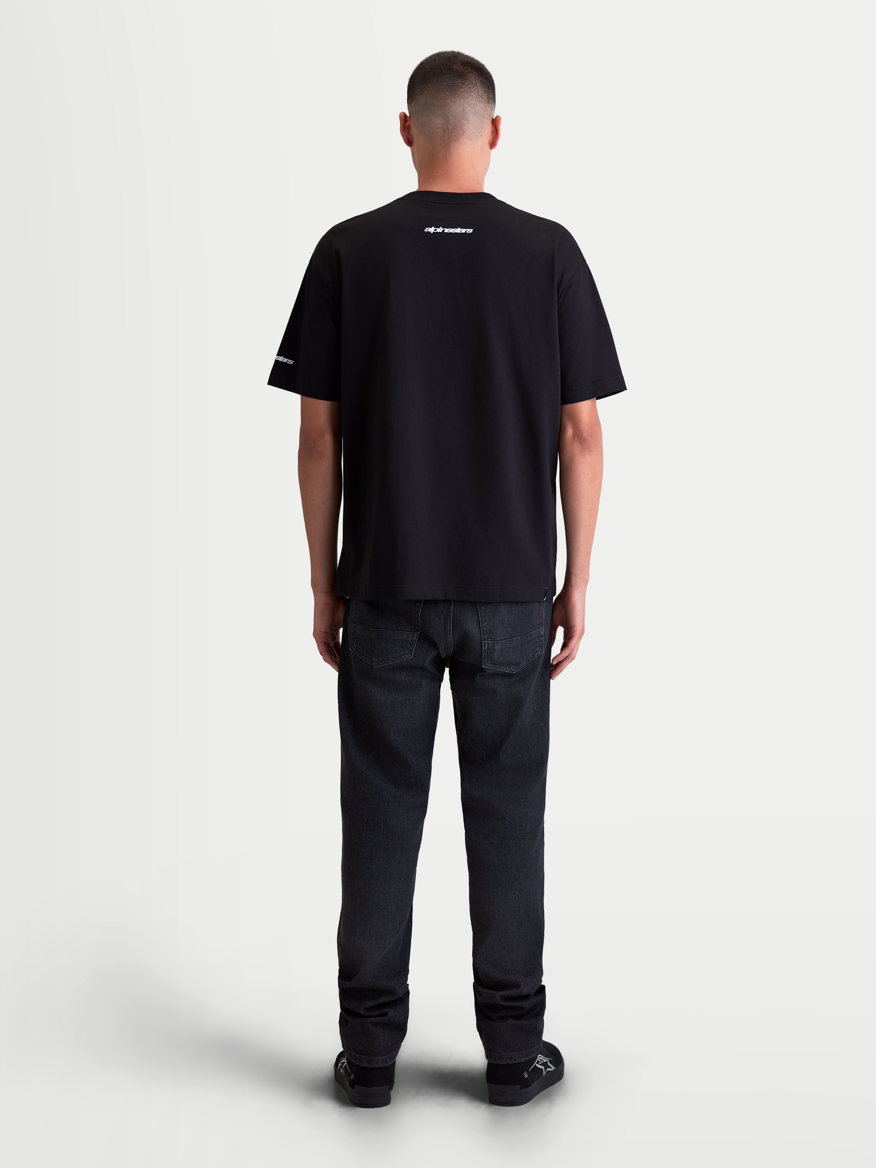 Alpinestars Mandate Oversized CSF T-shirt, kortærmet unisex-t-shirt, sort, 60/40 bomulds-polyesterblanding, set bagfra på model med hvid puff-print grafik på hals og ærme, afslappet oversized pasform.