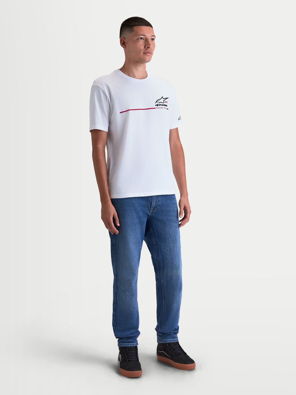 Alpinestars P1 CSF T-shirt, hvid herre sportswear t-shirt med korte ærmer, sort race-stribe logografik med blød finish på brystet, fremstillet i en behagelig bomuldsblanding til hverdagsbrug, herremodel iført t-shirten sammen med jeans.