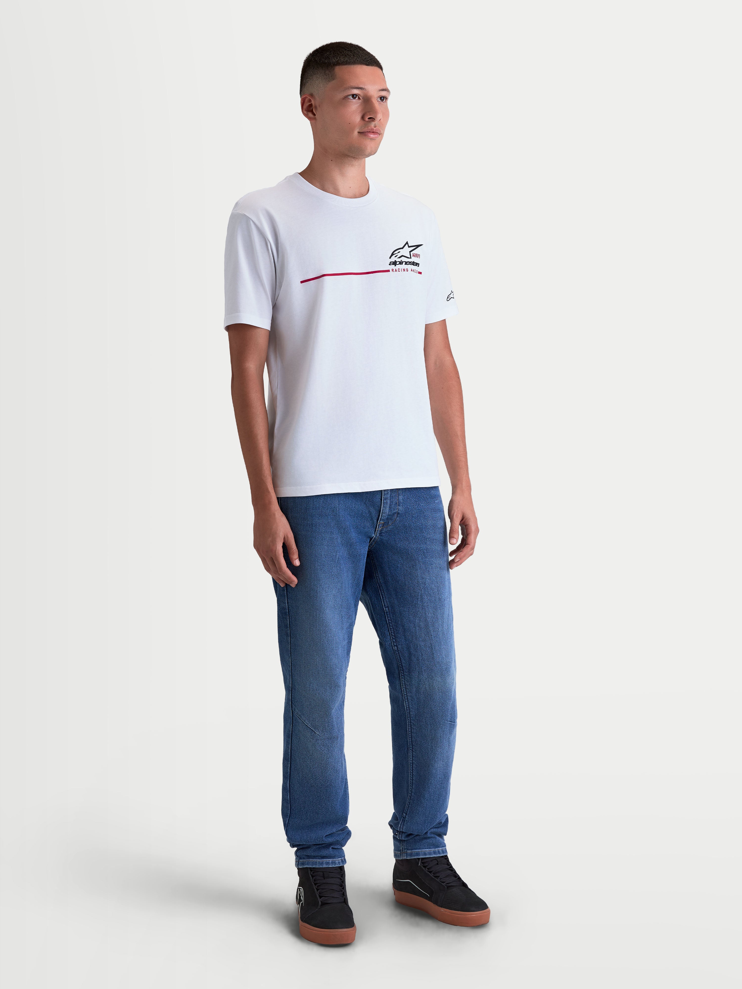 Alpinestars P1 CSF T-shirt, hvid herre sportswear t-shirt med korte ærmer, sort race-stribe logografik med blød finish på brystet, fremstillet i en behagelig bomuldsblanding til hverdagsbrug, herremodel iført t-shirten sammen med jeans.